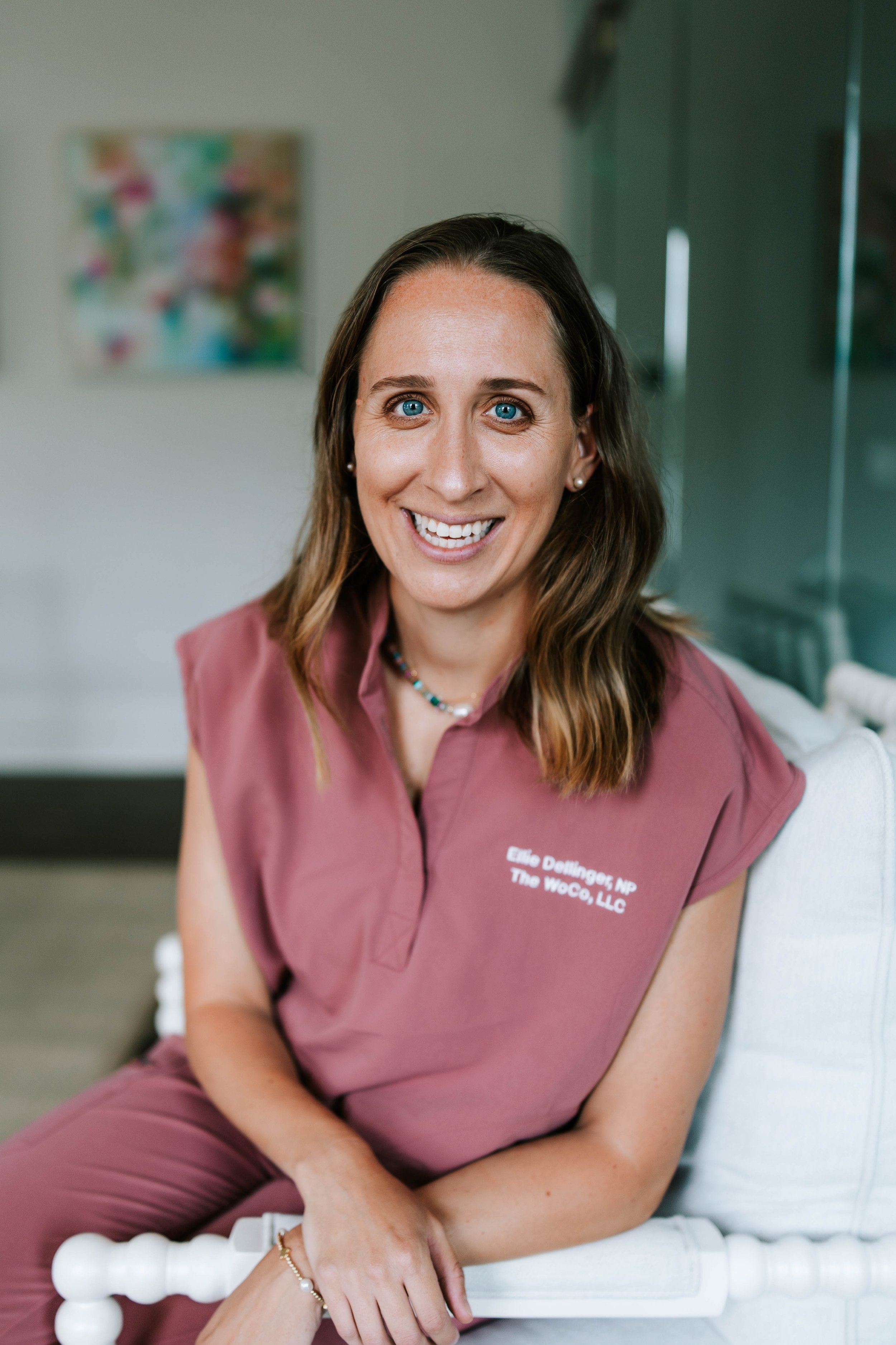 A woman smiling with crossed arms, wearing a pink medical scrub top with text indicating her name and title, standing against a plain light background. Women's Health Company, Athens, Oconee, Jefferson, Georgia Hormone Health