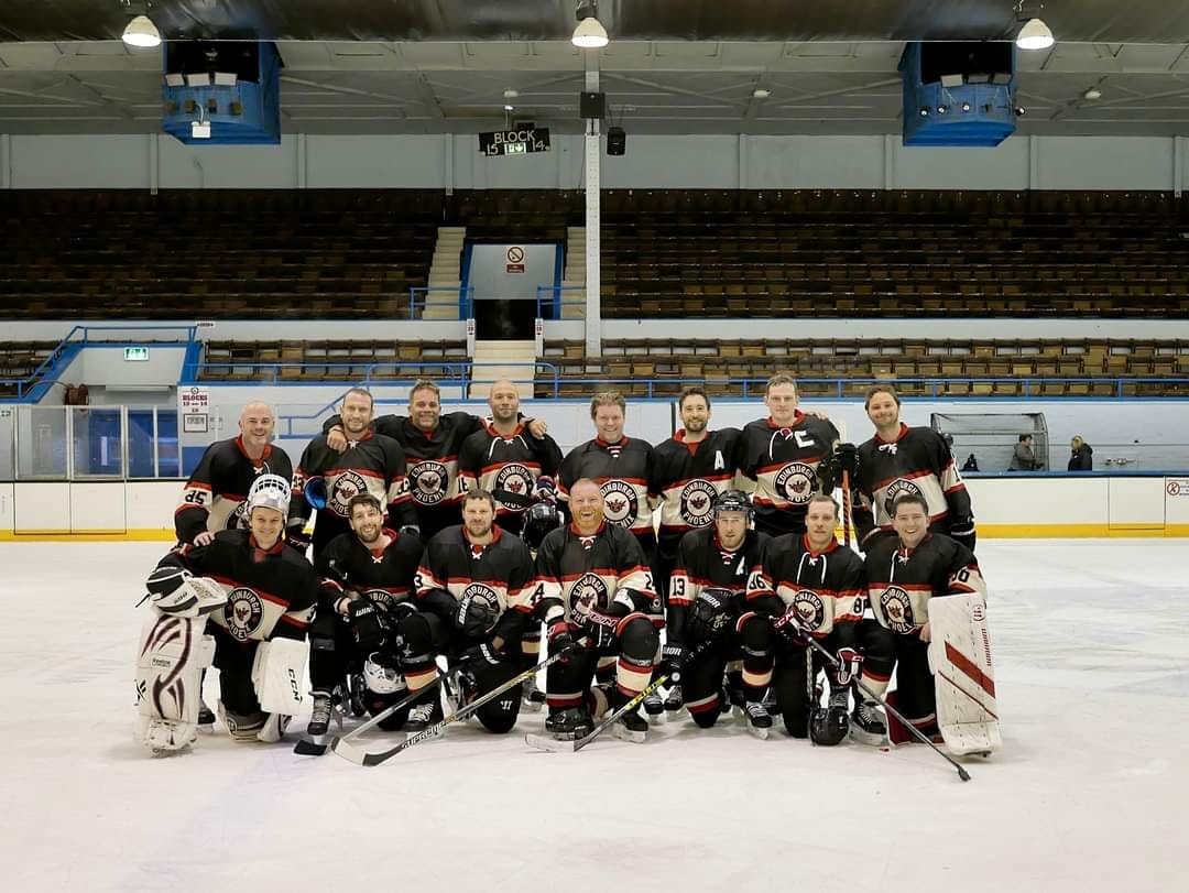 An ice hockey team in black and red uniforms posing for a team photo on the ice rink.