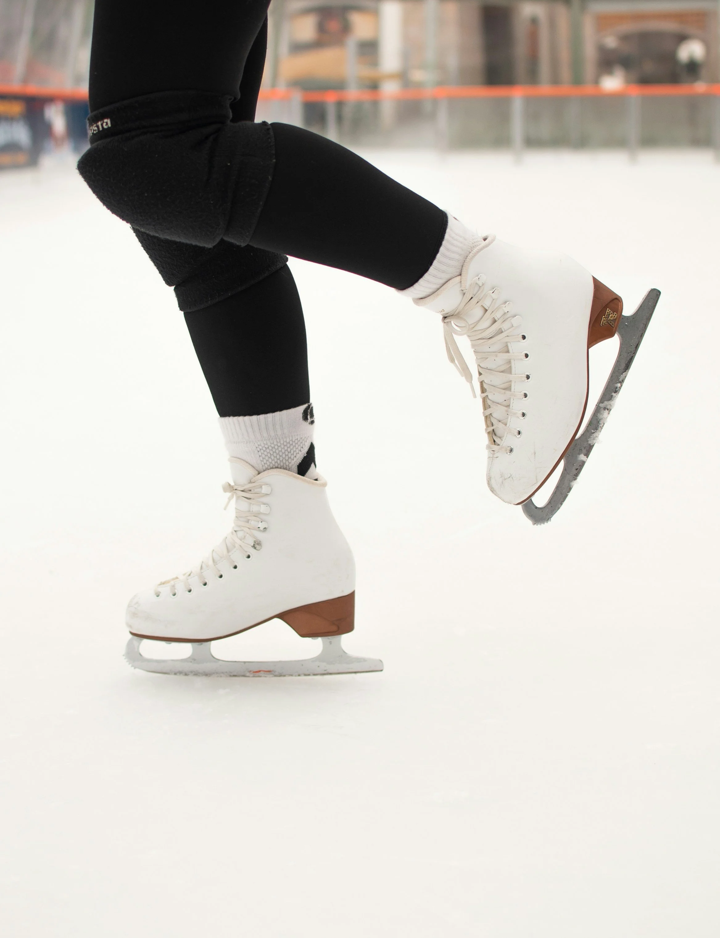 Close-up of white ice skates worn by a person on an ice rink, with the person slightly lifting one skate.