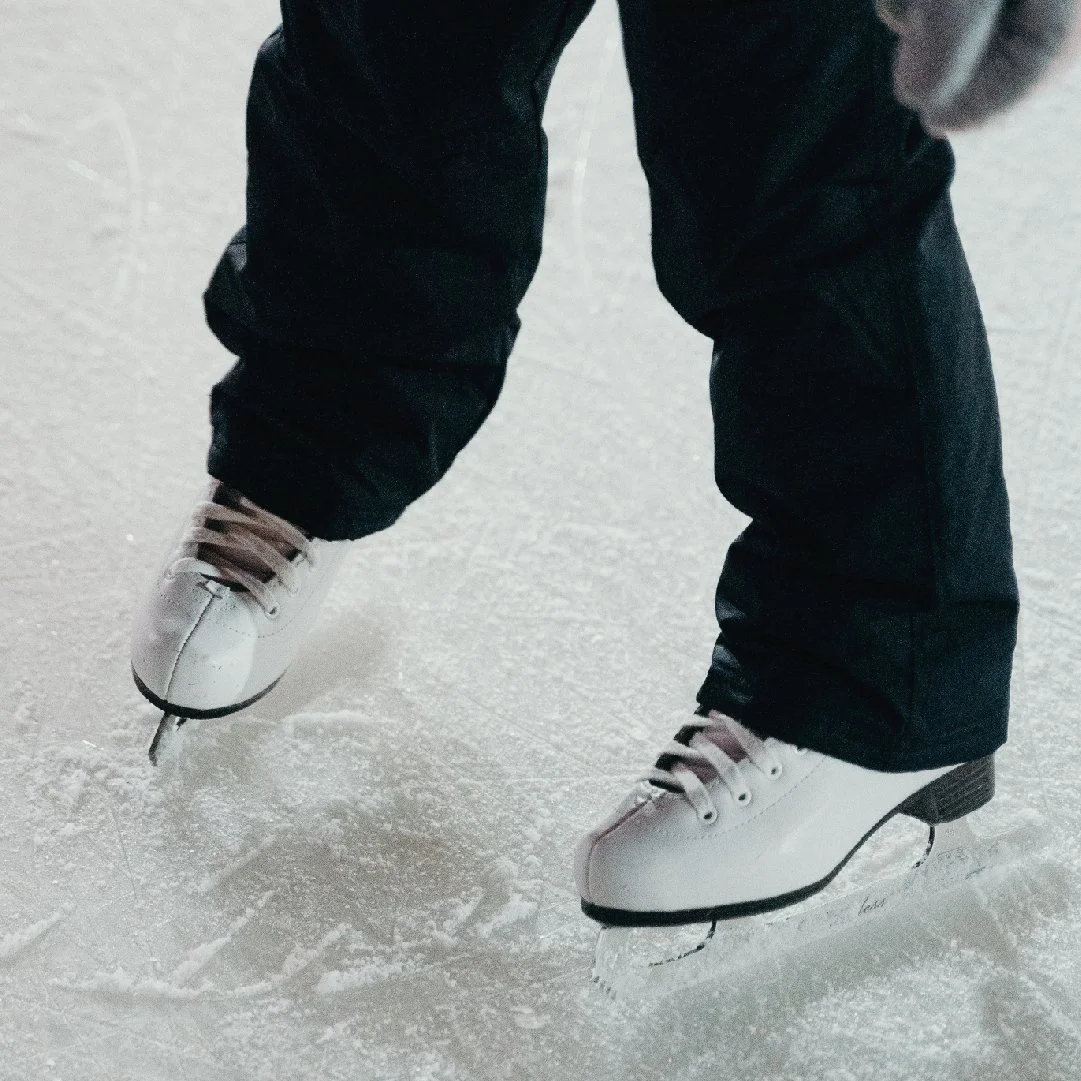 Person wearing white ice skates on ice rink, black pants, skating