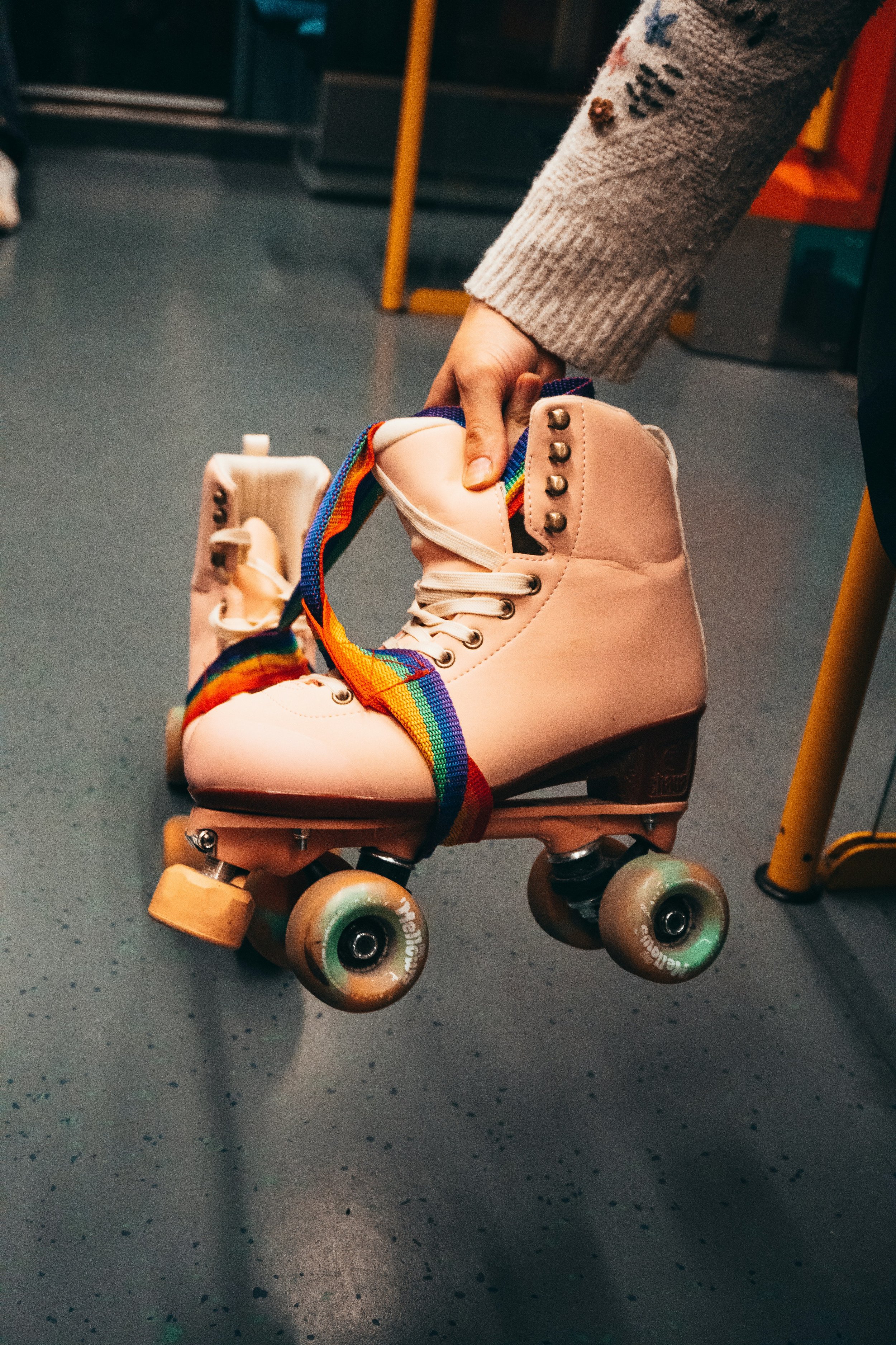 A person holding a vintage pink roller skate with rainbow-colored laces.