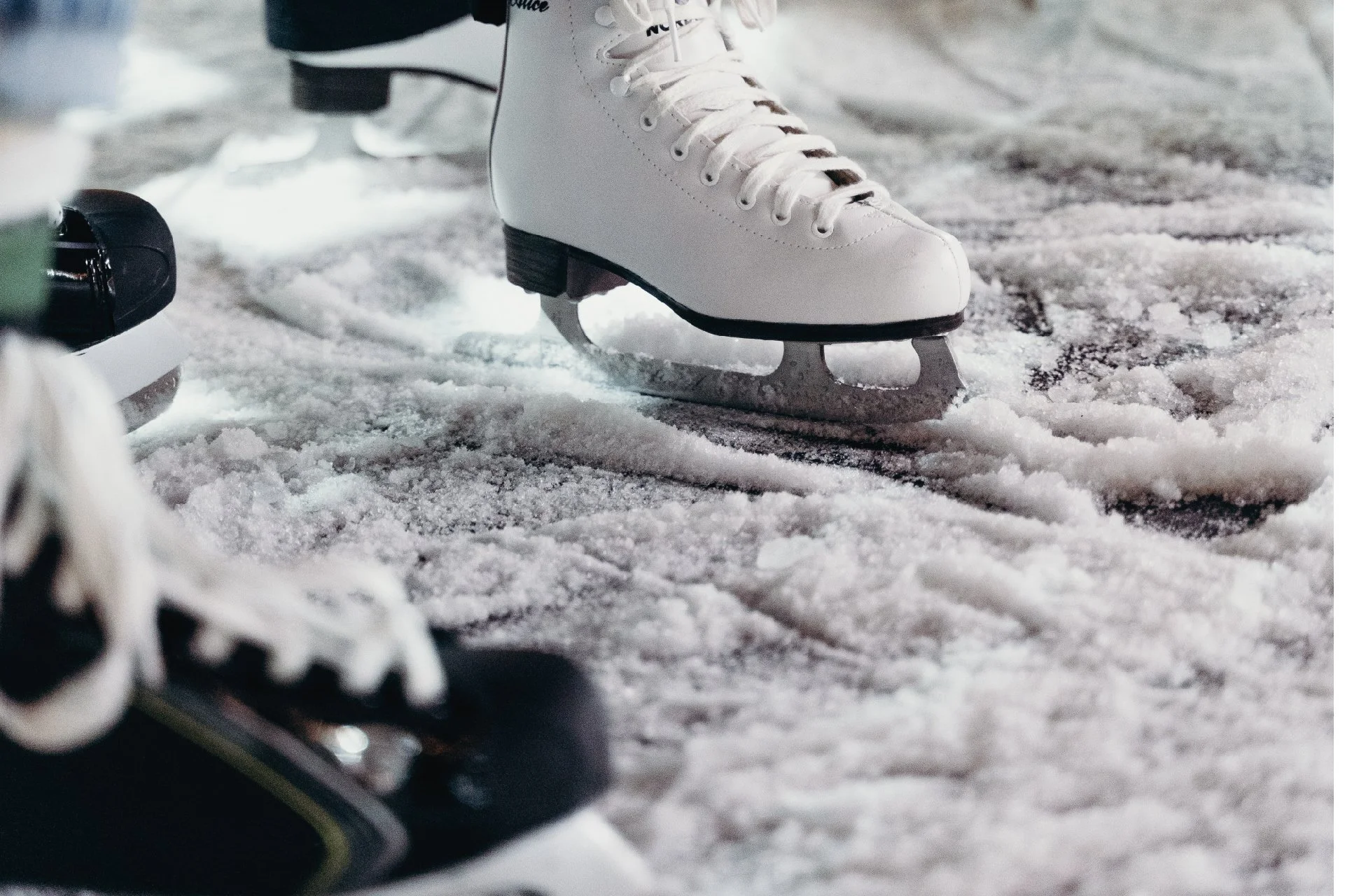 Close-up of white ice skates on ice rink, with black soles and laces, in a skating rink setting.