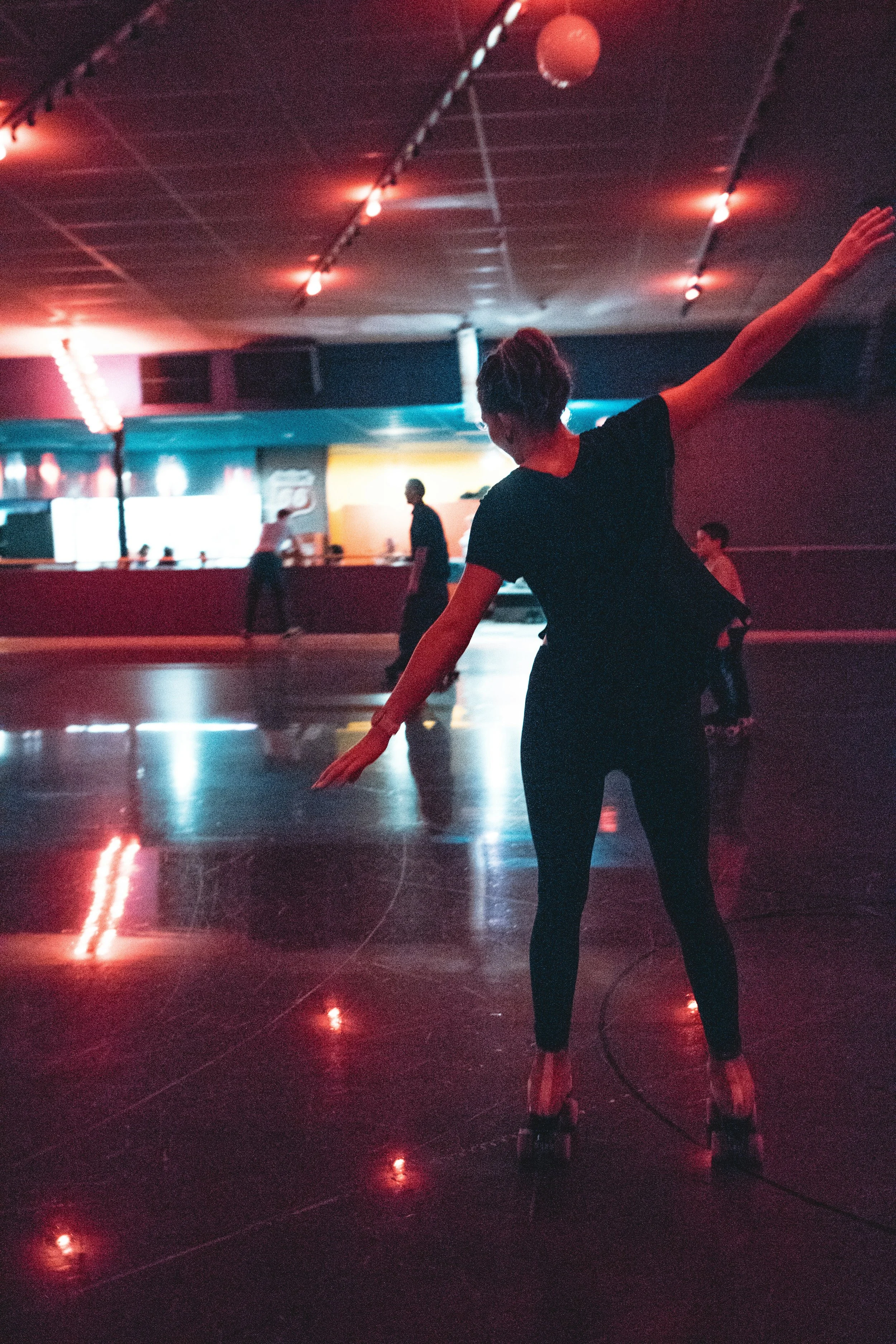 A woman roller skating in a dark, colorful indoor roller rink with neon lights and a large open space.