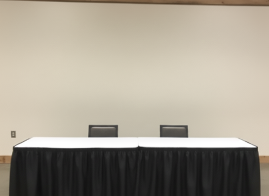 Empty table with black tablecloth and two chairs in front of a blank wall.