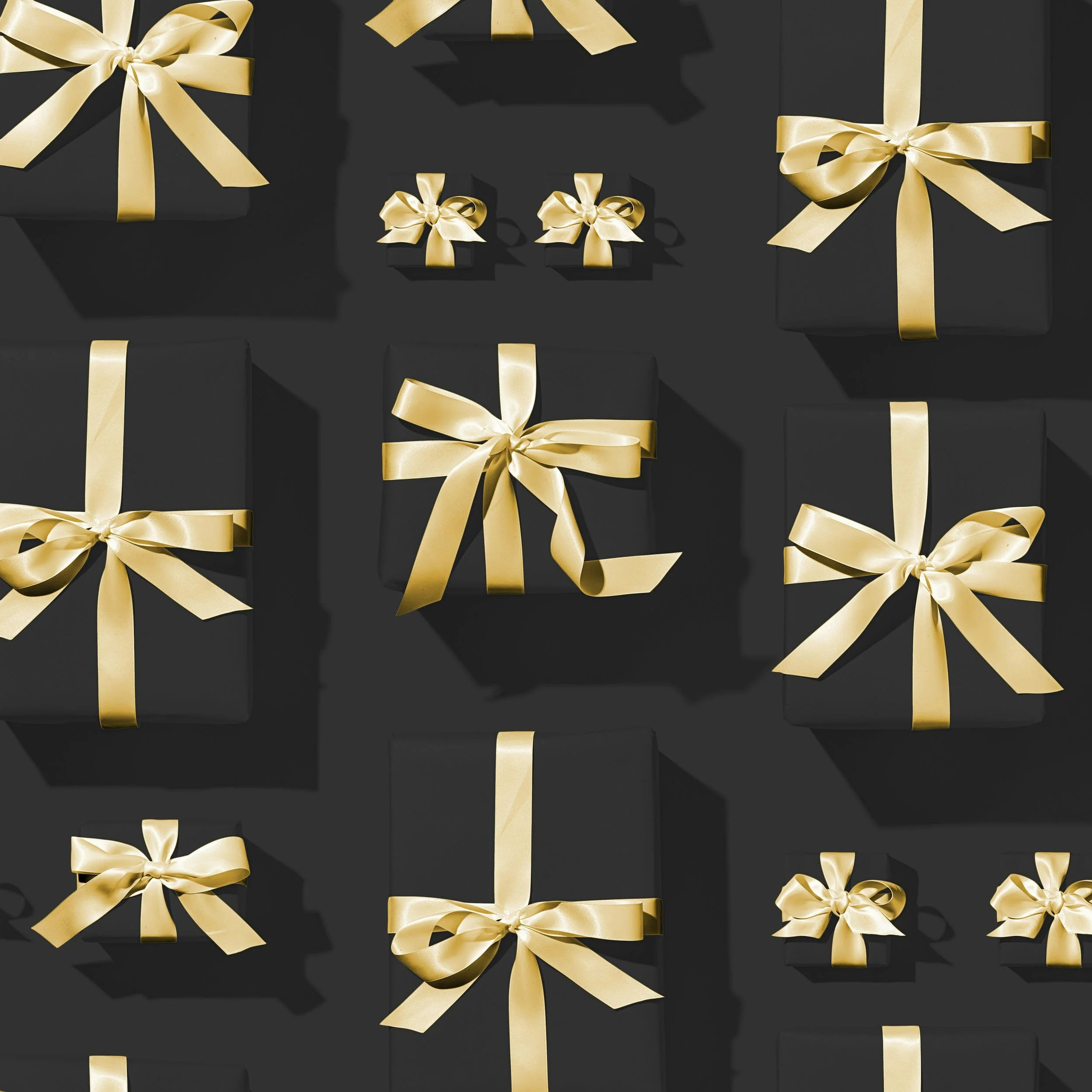 Multiple black gift boxes wrapped with gold satin ribbons and bows, arranged on a black surface with shadows.