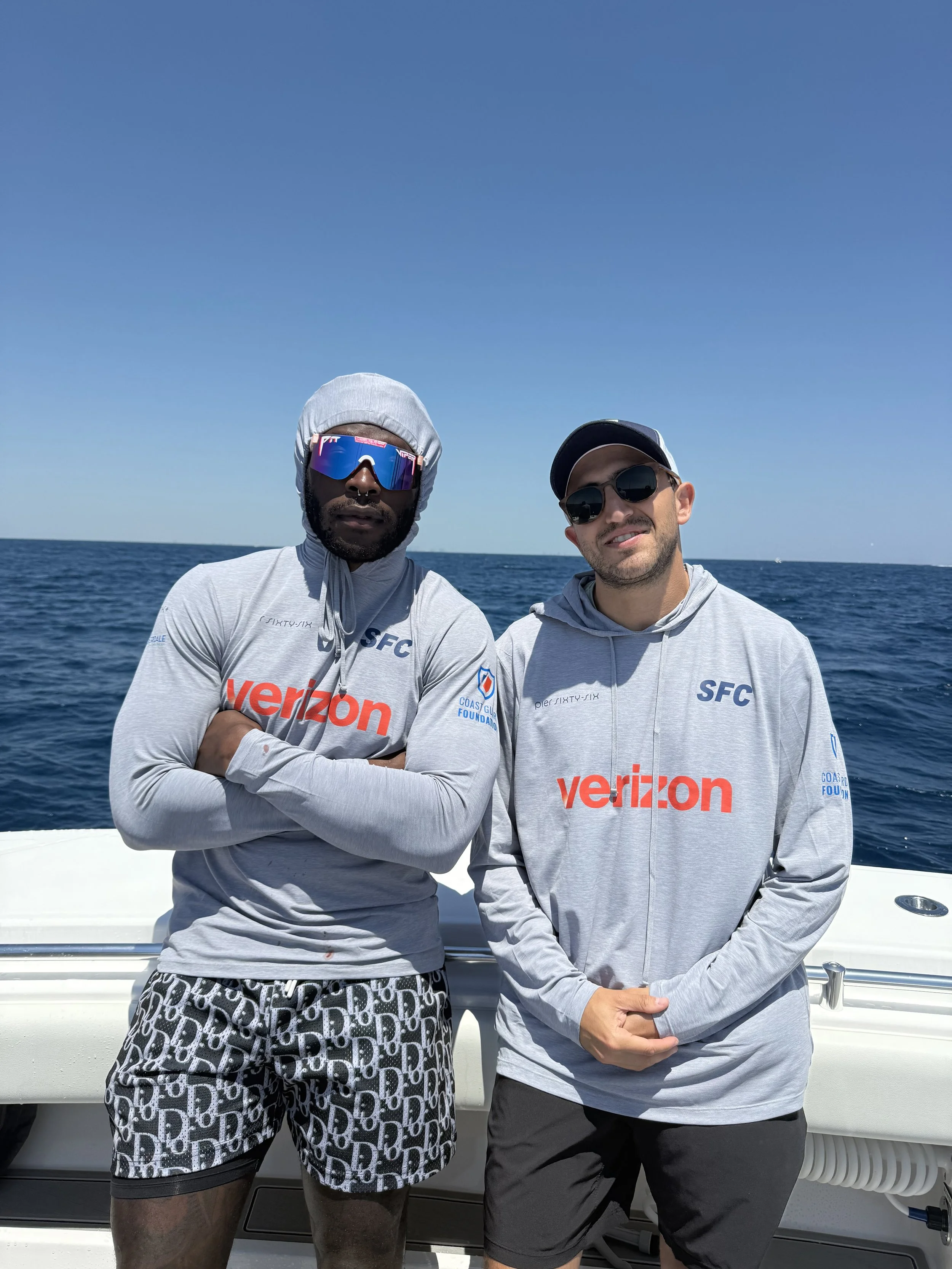 Two men in athletic gear on a boat, with ocean and clear sky in the background.