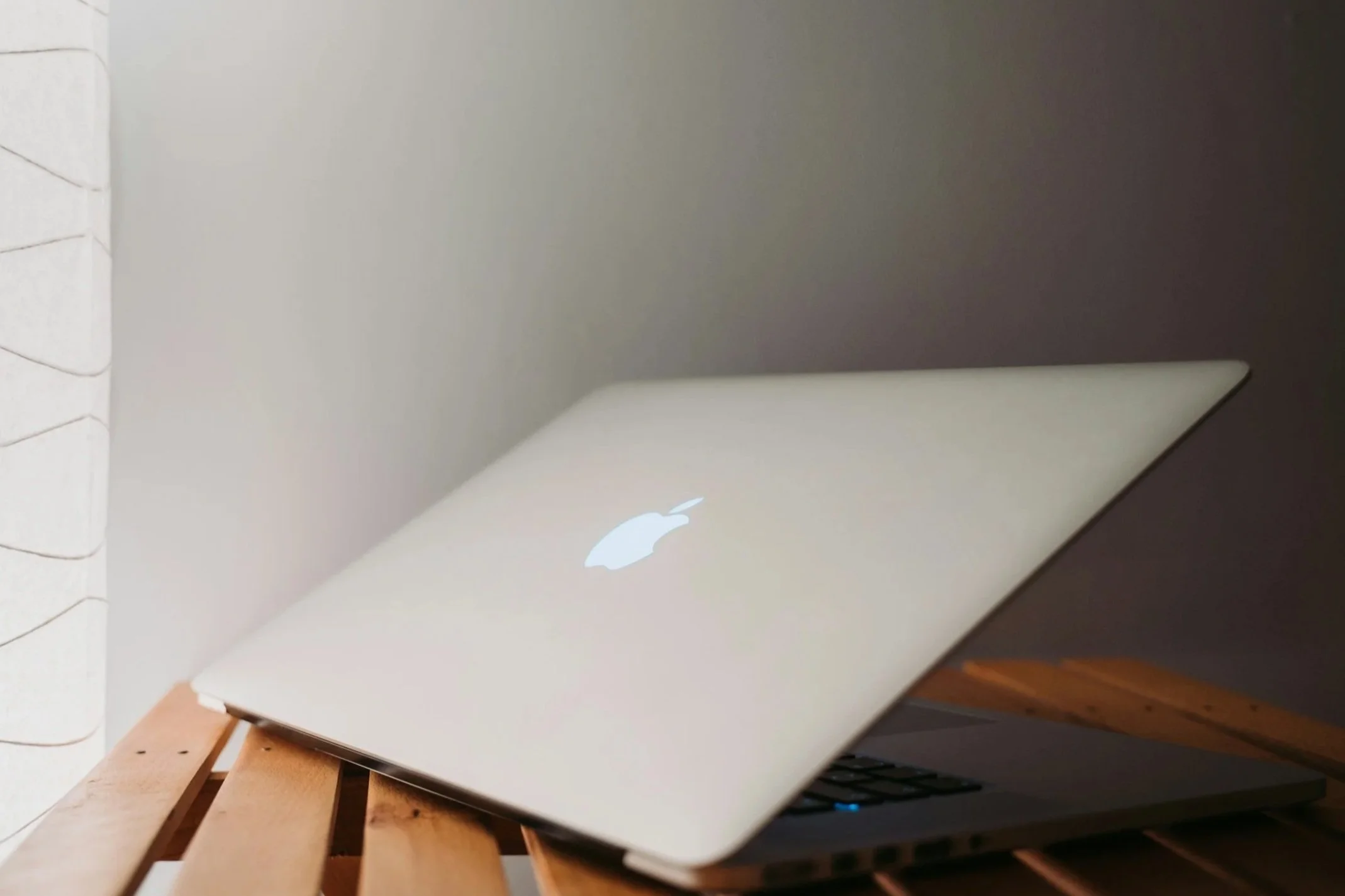 Close-up of a closed silver Apple MacBook on a wooden table with a dark wall in the background.