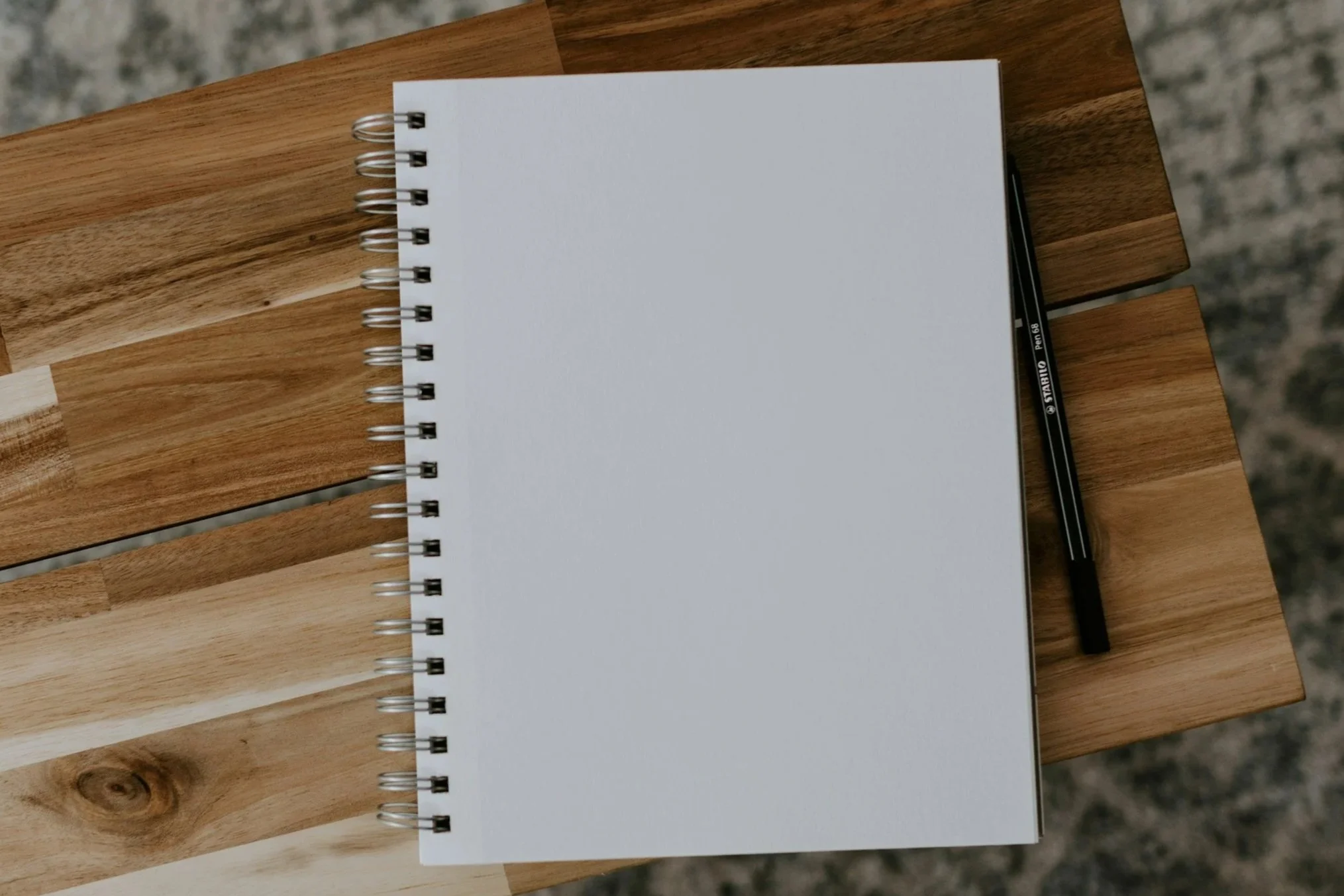 Open blank spiral notebook on wooden table with black pen.
