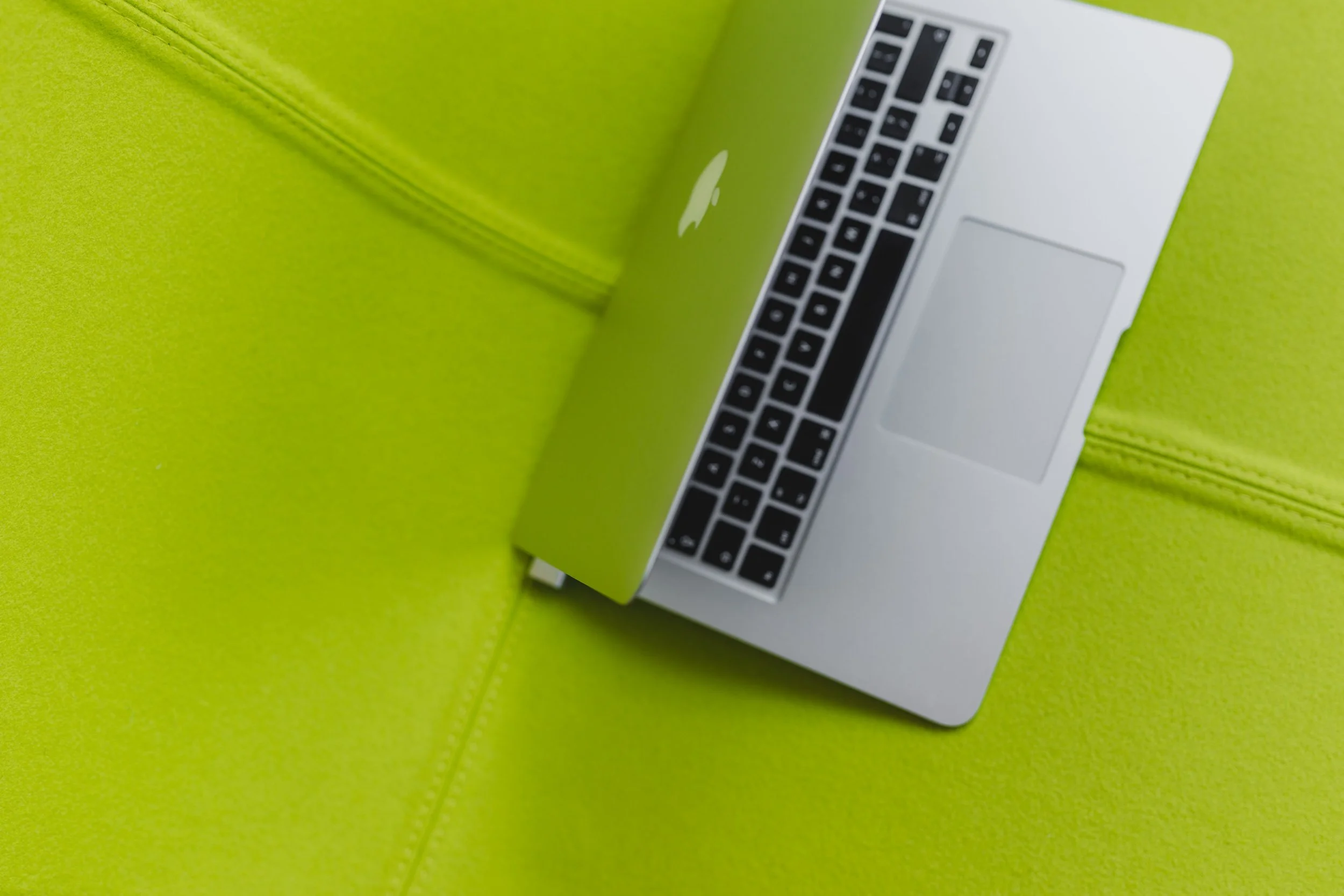 Silver MacBook laptop opened on a bright green cushioned surface with green fabric and stitching.