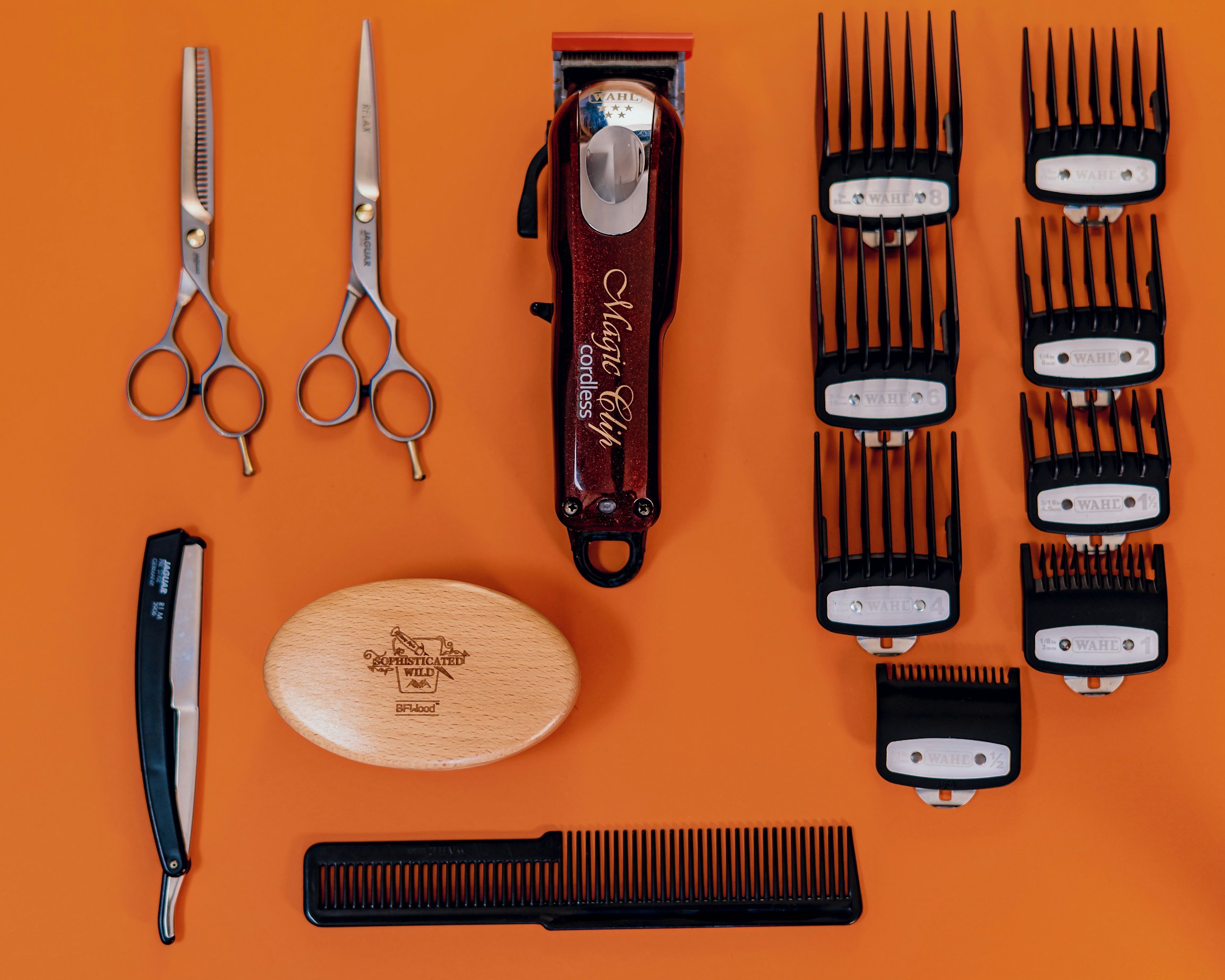 A collection of hairdressing tools on an orange background, including scissors, hair clippers, and clipper guards.