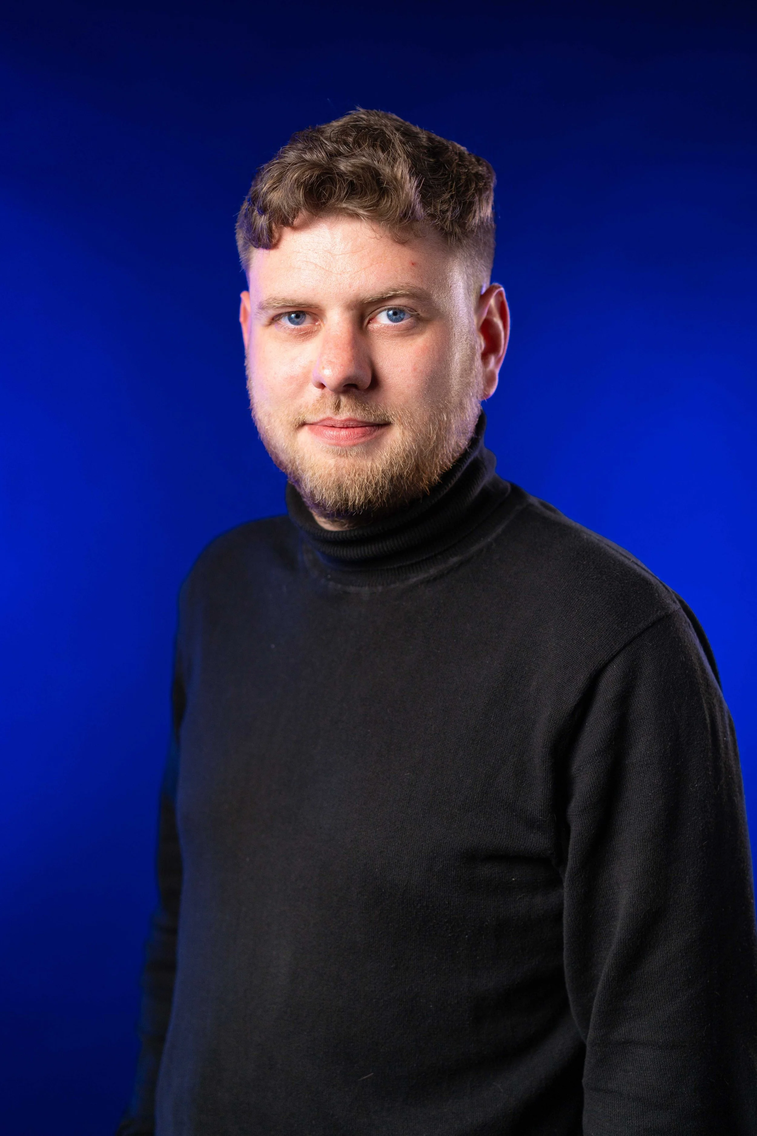Portrait d'un jeune homme portant un pull noir, avec un fond bleu foncé.