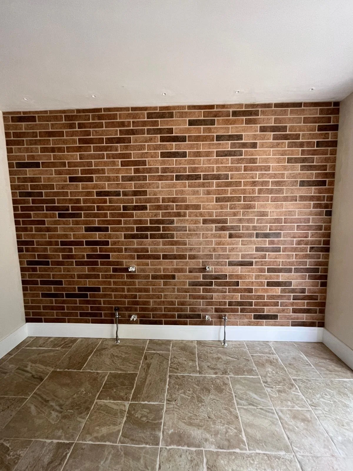 Empty room with a brick accent wall, concrete tiled floor, and electrical outlets without covers.