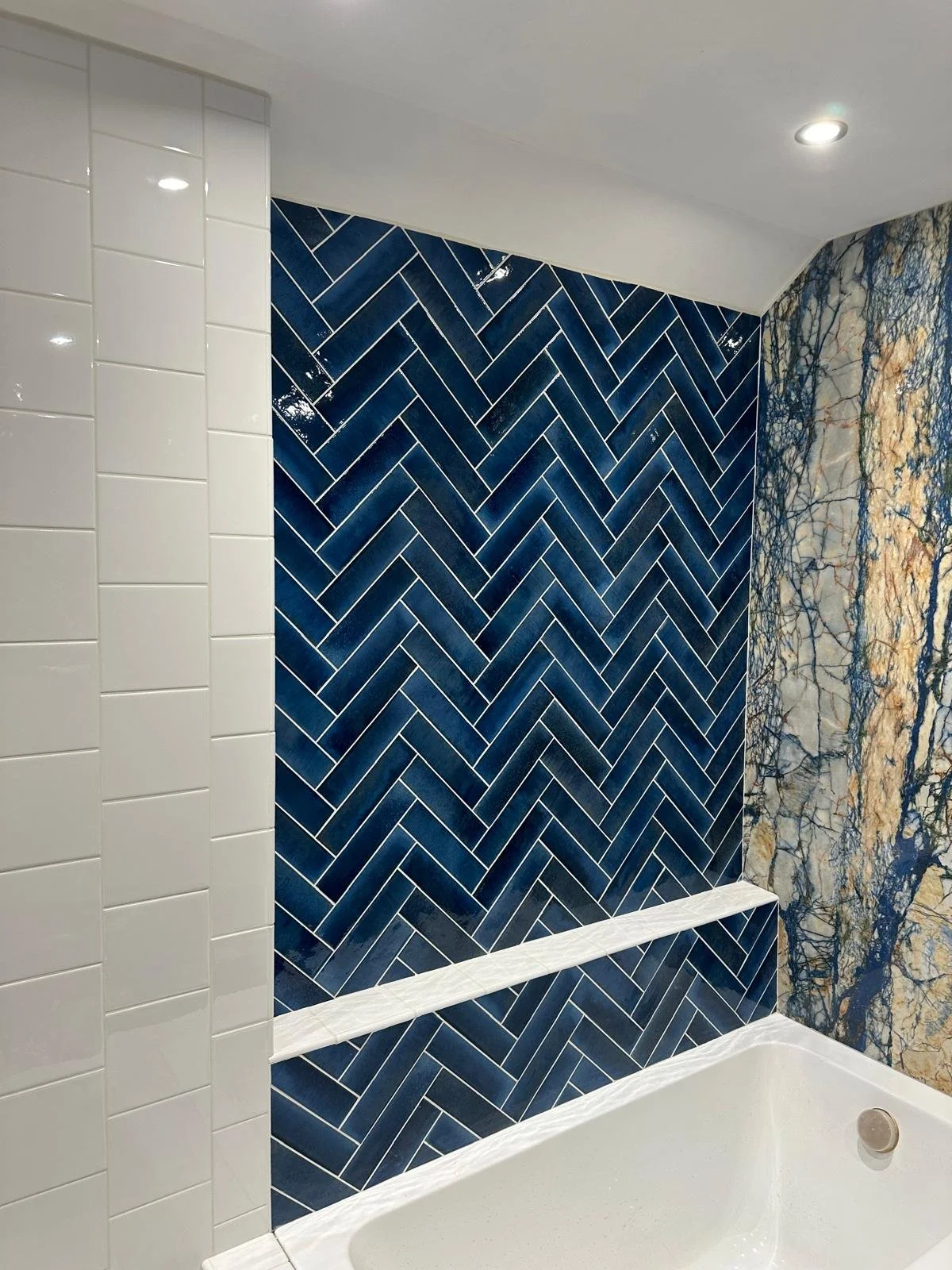 Bathroom wall with various tiles, including a large dark blue herringbone pattern, white subway tiles, and a textured marble-like pattern with blue and beige tones.