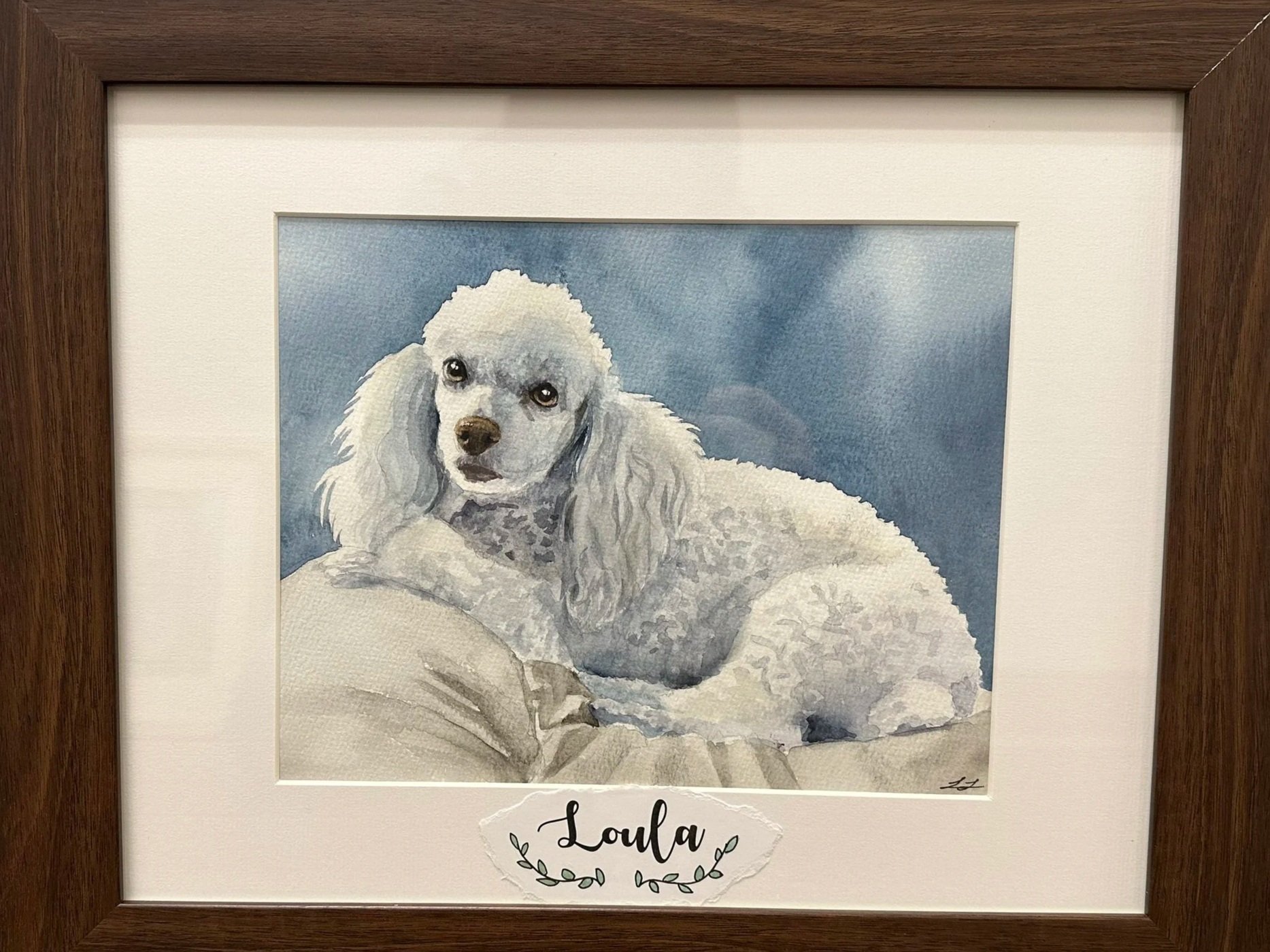 Watercolor painting of a white poodle dog lying on a blanket against a blue sky background, framed with a wooden border.