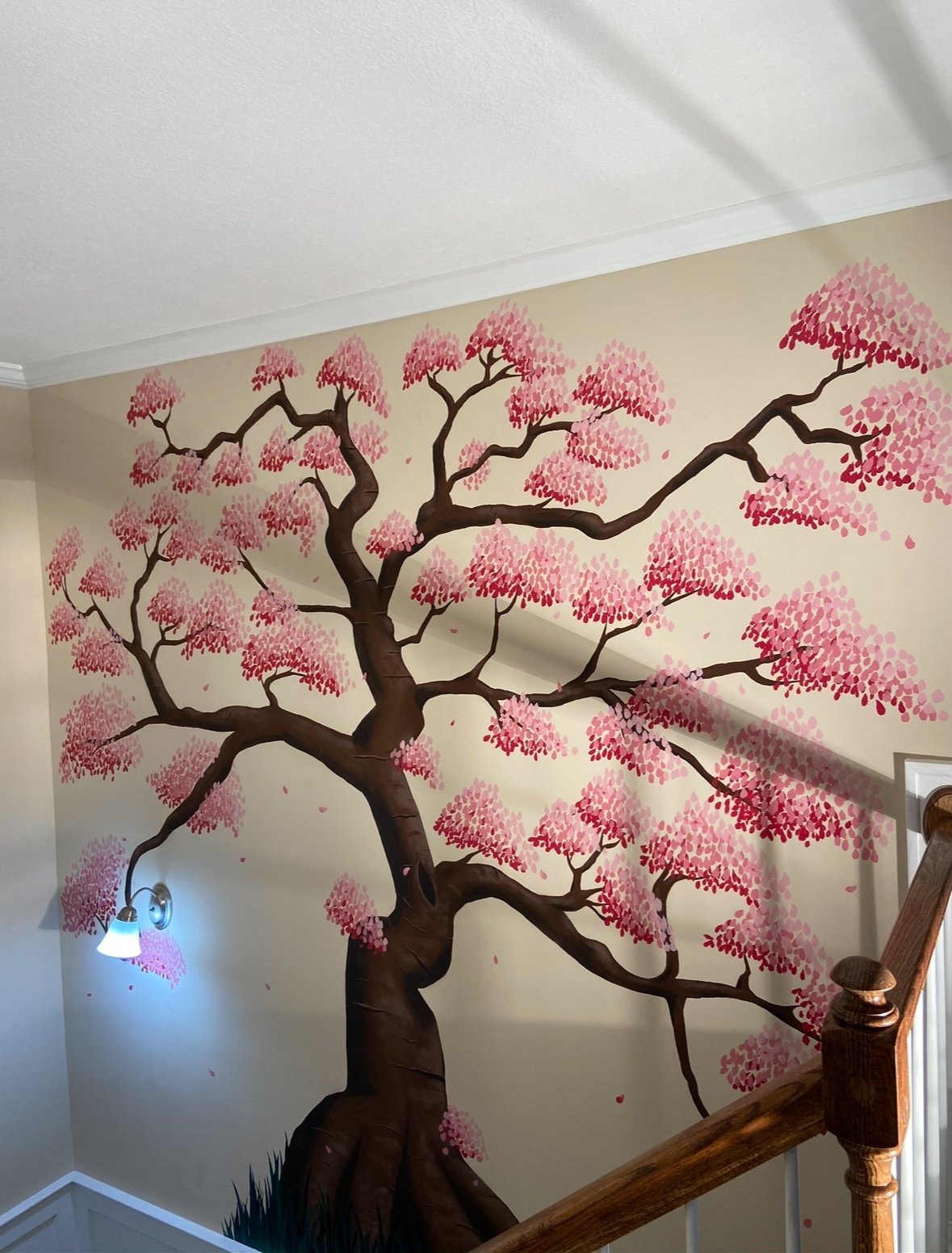 Interior wall mural of a large pink blossoming tree with dark brown trunk and branches, painted on a beige wall near a staircase.