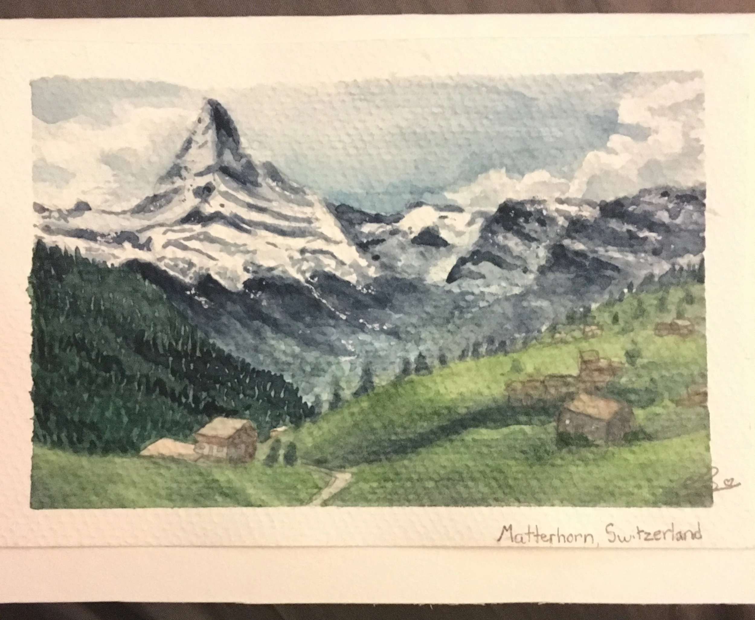 A watercolor painting of Matterhorn mountain in Switzerland with a snowy peak, green foreground, and a cloudy sky.