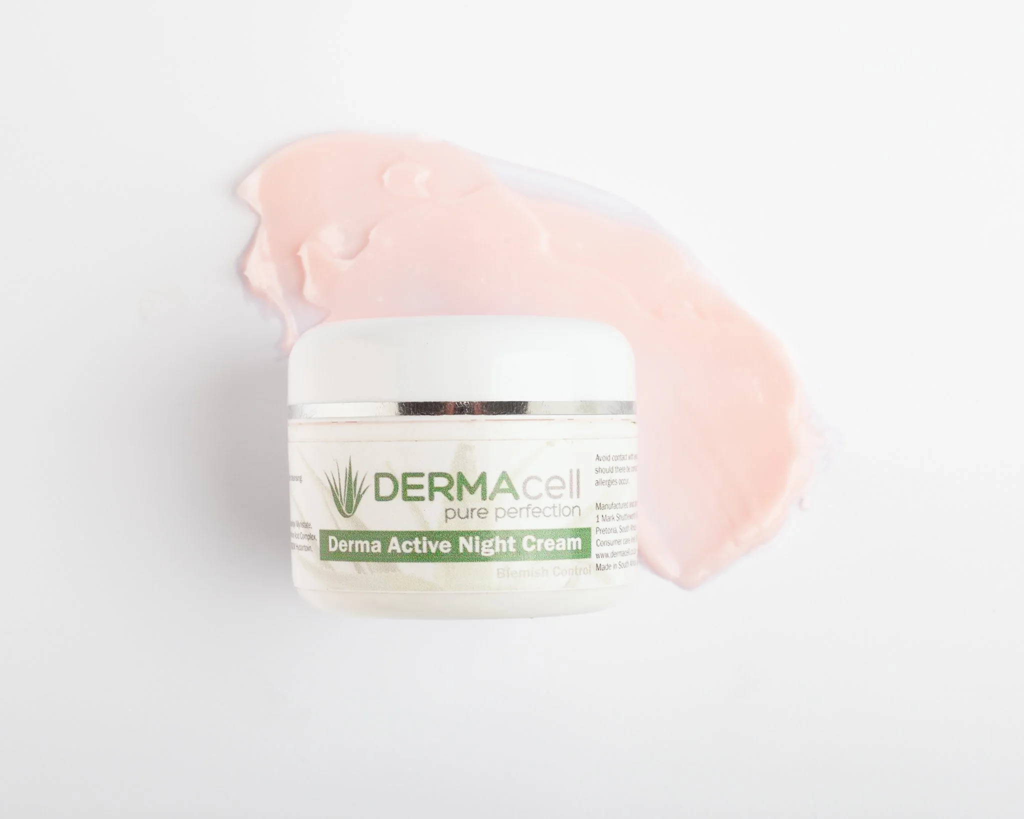 Container of Derma Active Night Cream with pink cream spilled around it on a white surface.