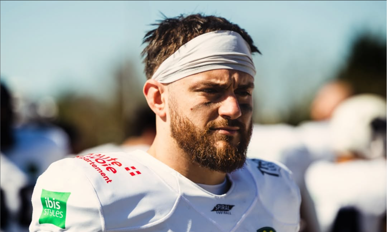 Un joueur de football américain avec un bandeau blanc sur la tête, portant un maillot blanc avec des logos publicitaires, regardant pensif lors d'un match.
