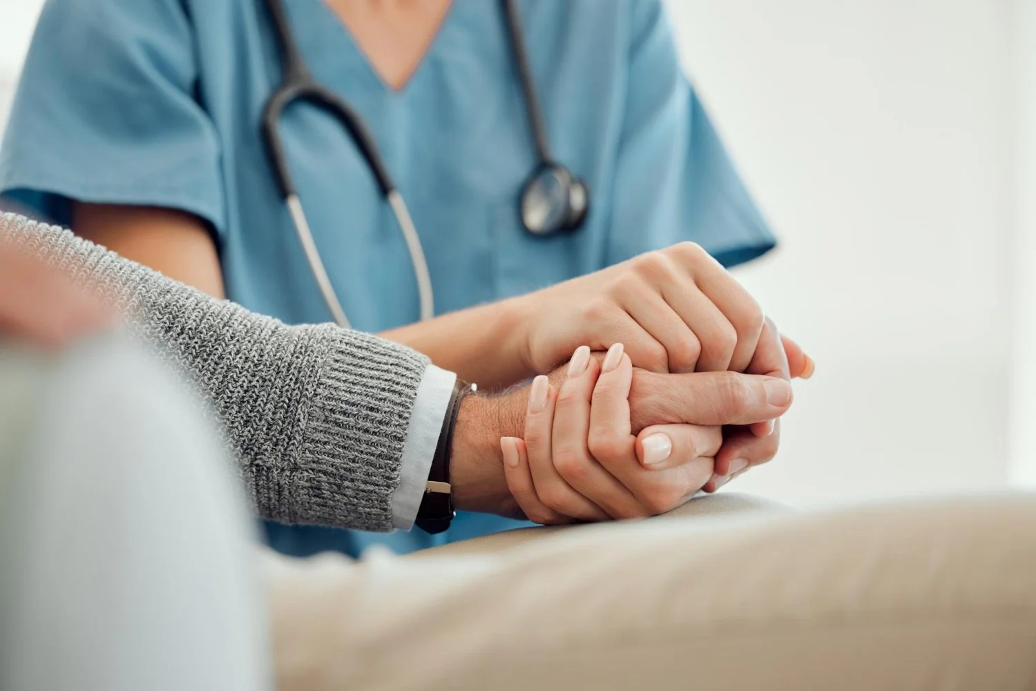 A healthcare professional holding a patient's hand during a consultation or examination.