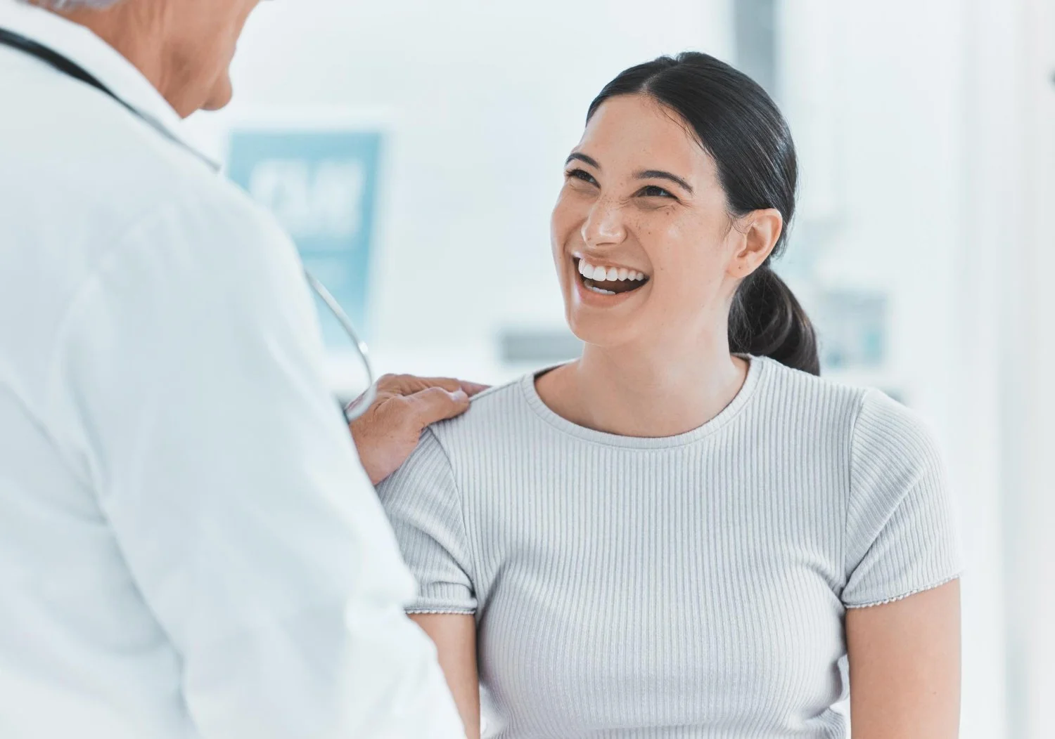 A woman smiling happily at a doctor in a bright medical office, during a check-up or vaccination.
