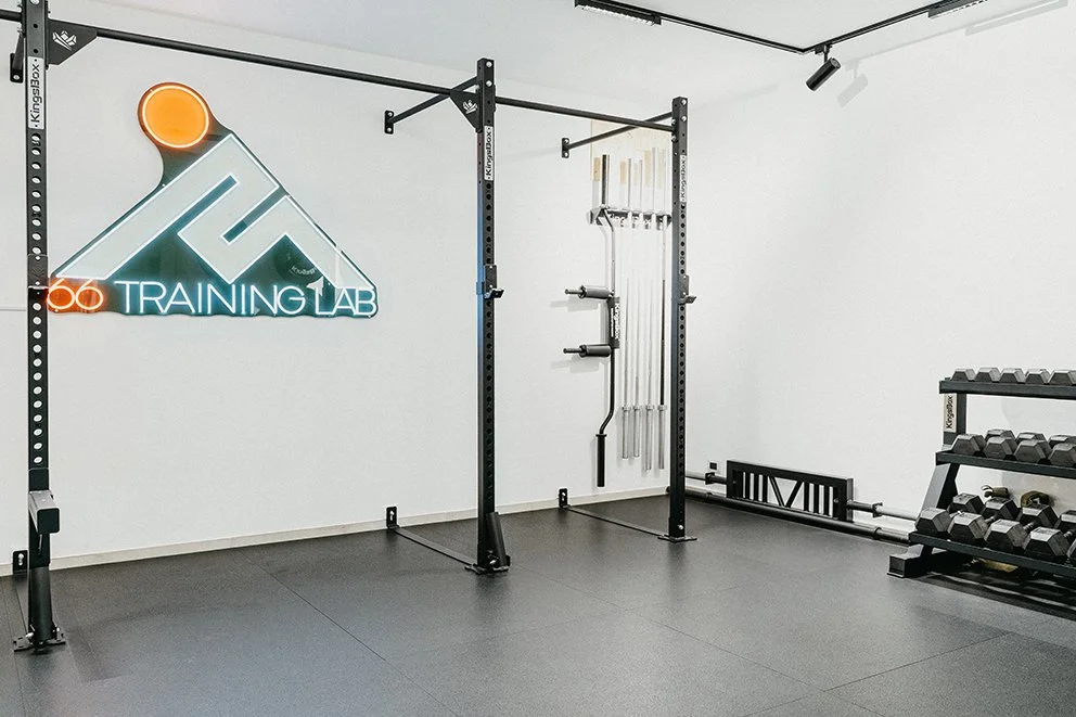 Sala di allenamento con attrezzi da palestra, pesi e una parete con attrezzature per il fitness, e un'illuminazione moderna con logo luminoso 'Training Lab' sulla parete a sinistra.