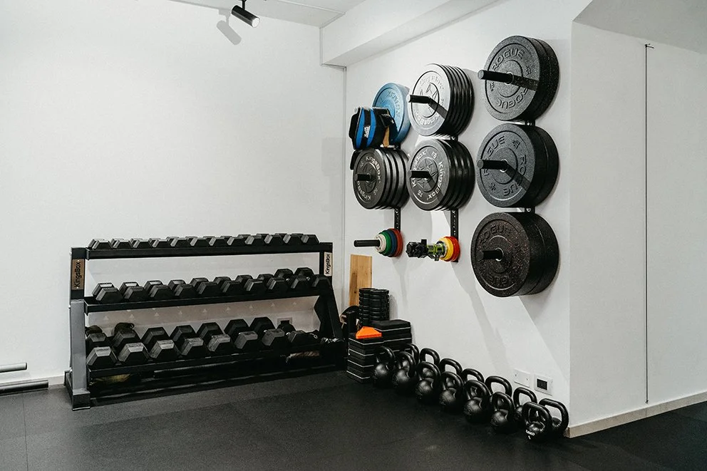 Attrezzature da palestra con manubri, kettlebell, dischi ponderati e accessori per allenamento in uno spazio dedicato alla boxing o strength training.