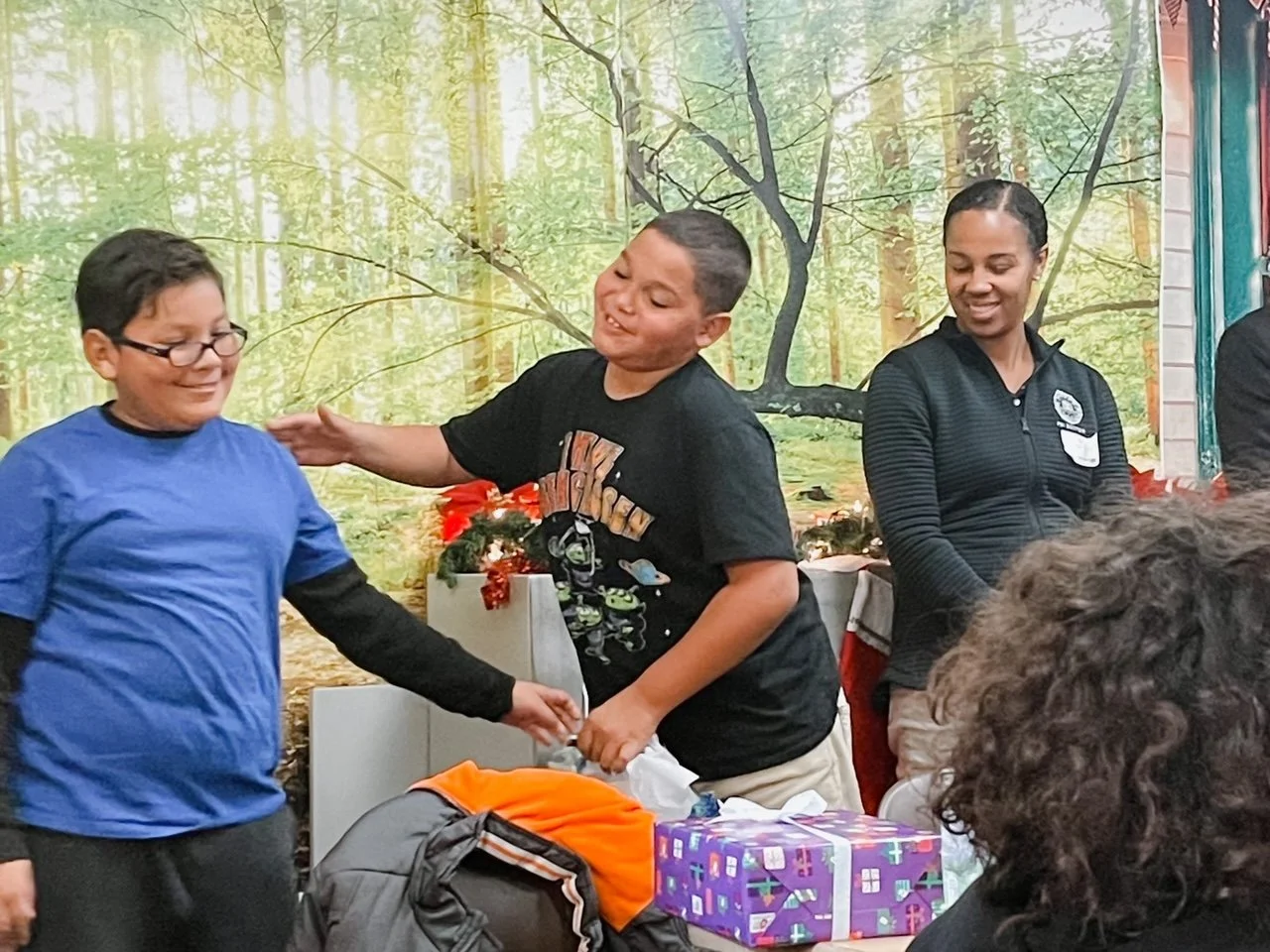 Children and adults celebrating with gifts in a decorated room featuring a forest mural background.