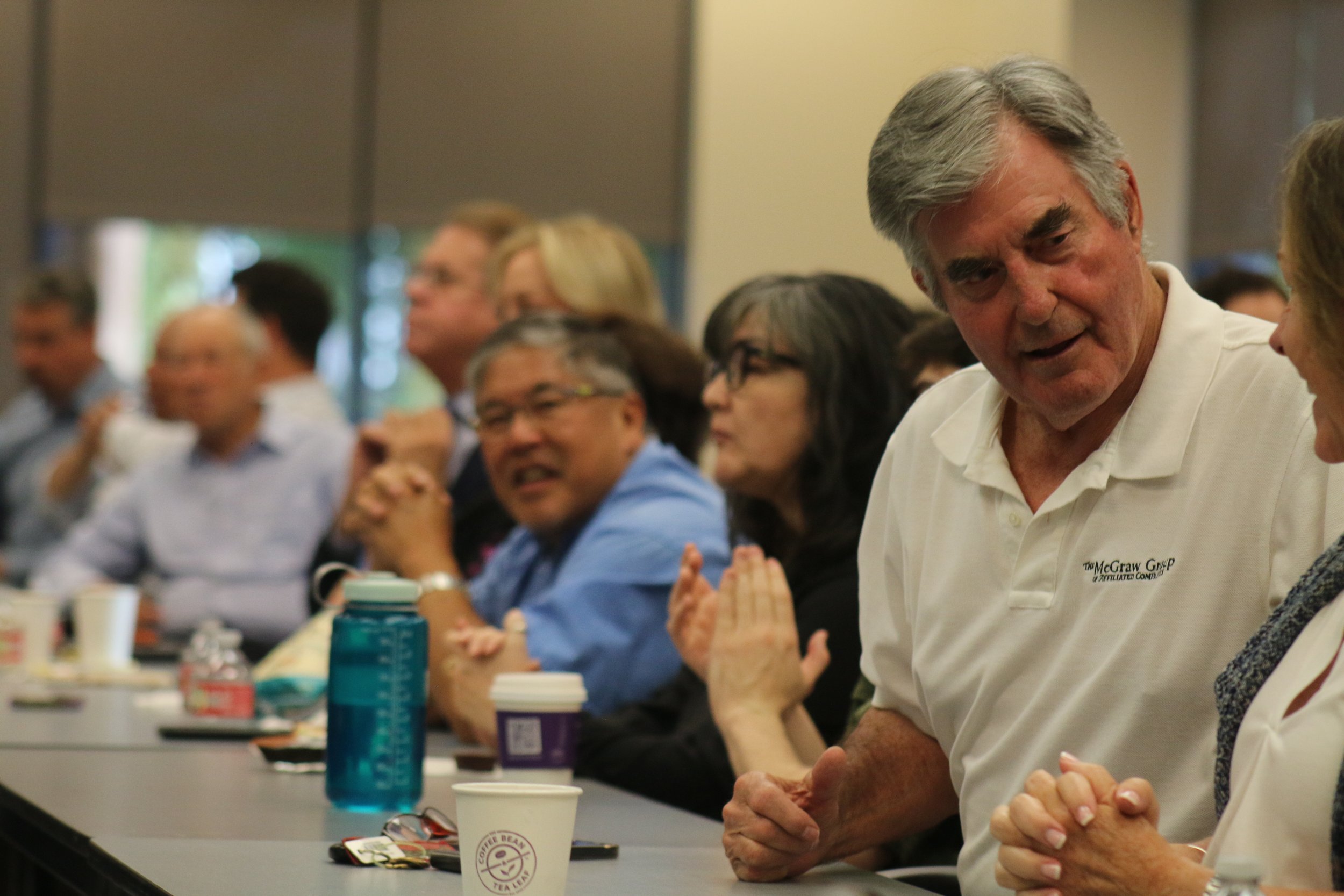 A group of people sitting at a conference table engaged in conversation, with cups, bottles, and papers in front of them.
