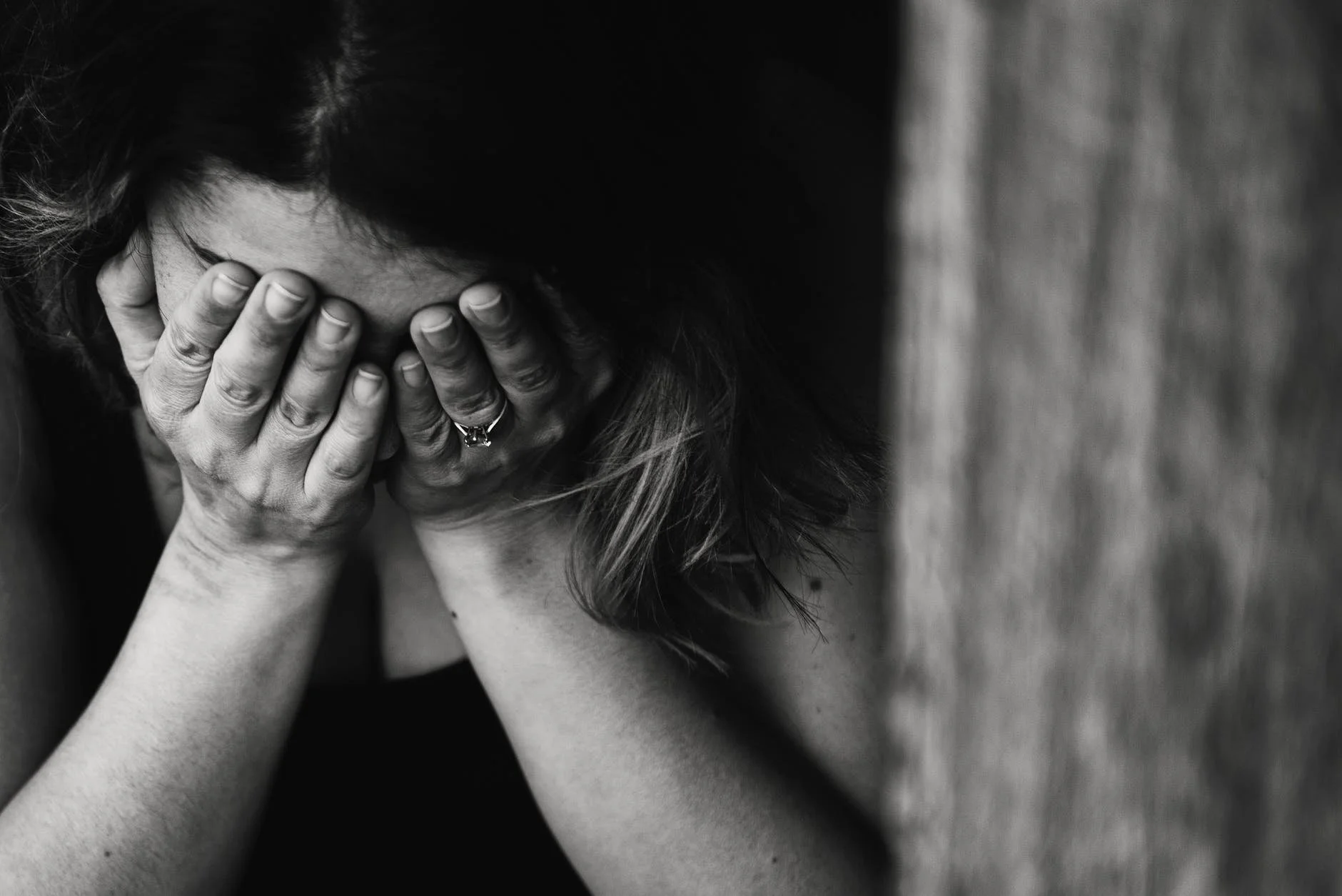 A woman covering her face with her hands, appearing distressed, in black and white.
