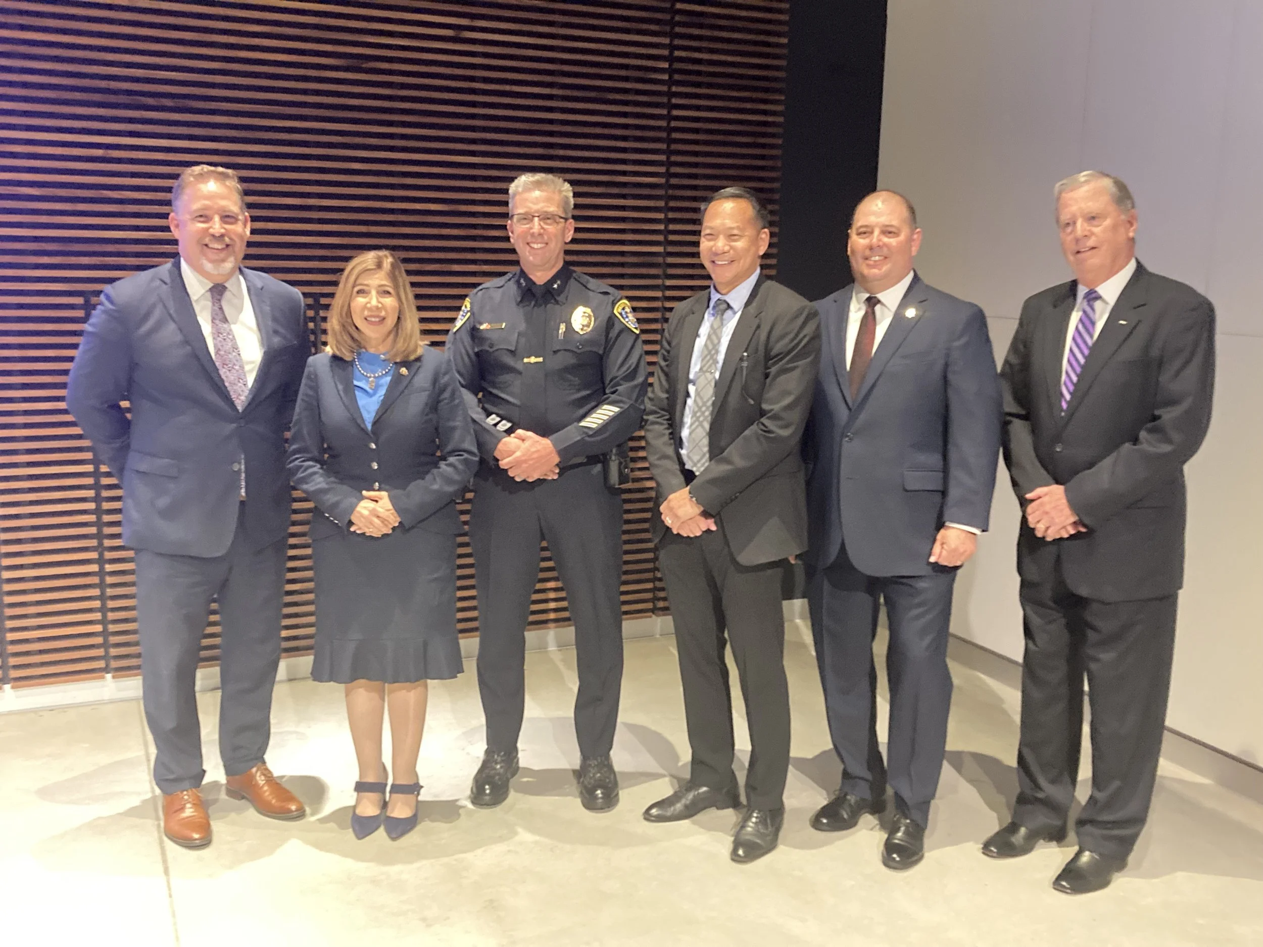 Seven professionals standing in a line at an indoor event, with a wooden wall backdrop.