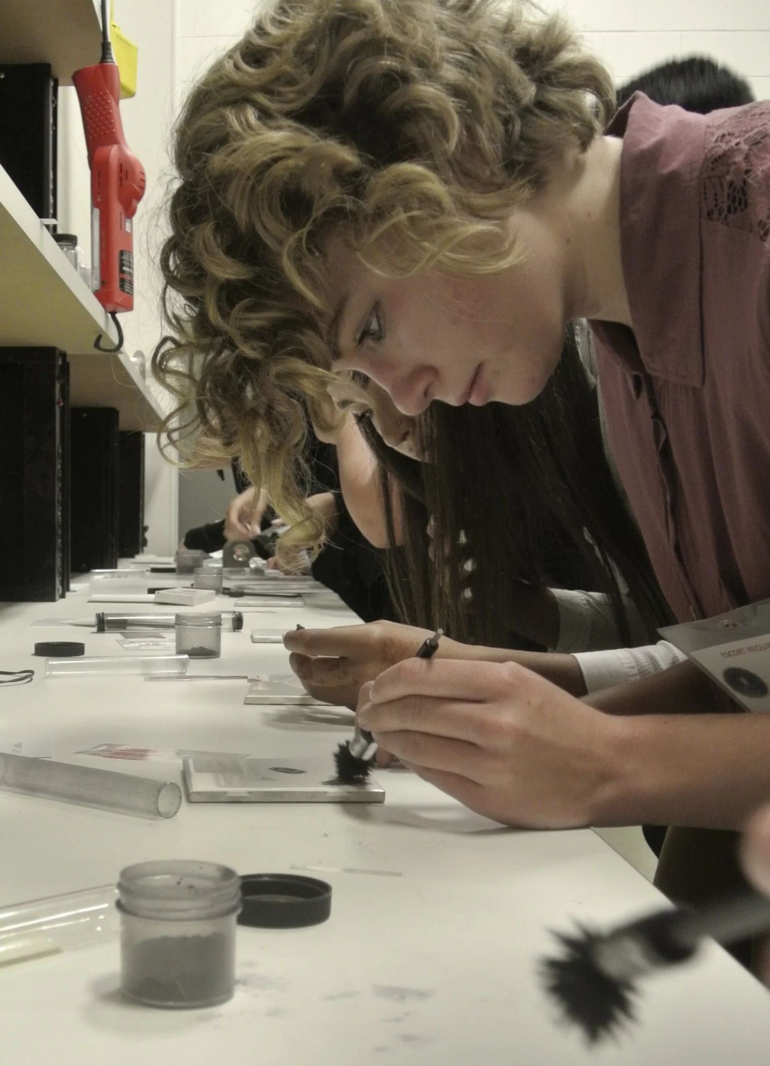 People working on forensic or evidence analysis with microscopes and tools on a long table.