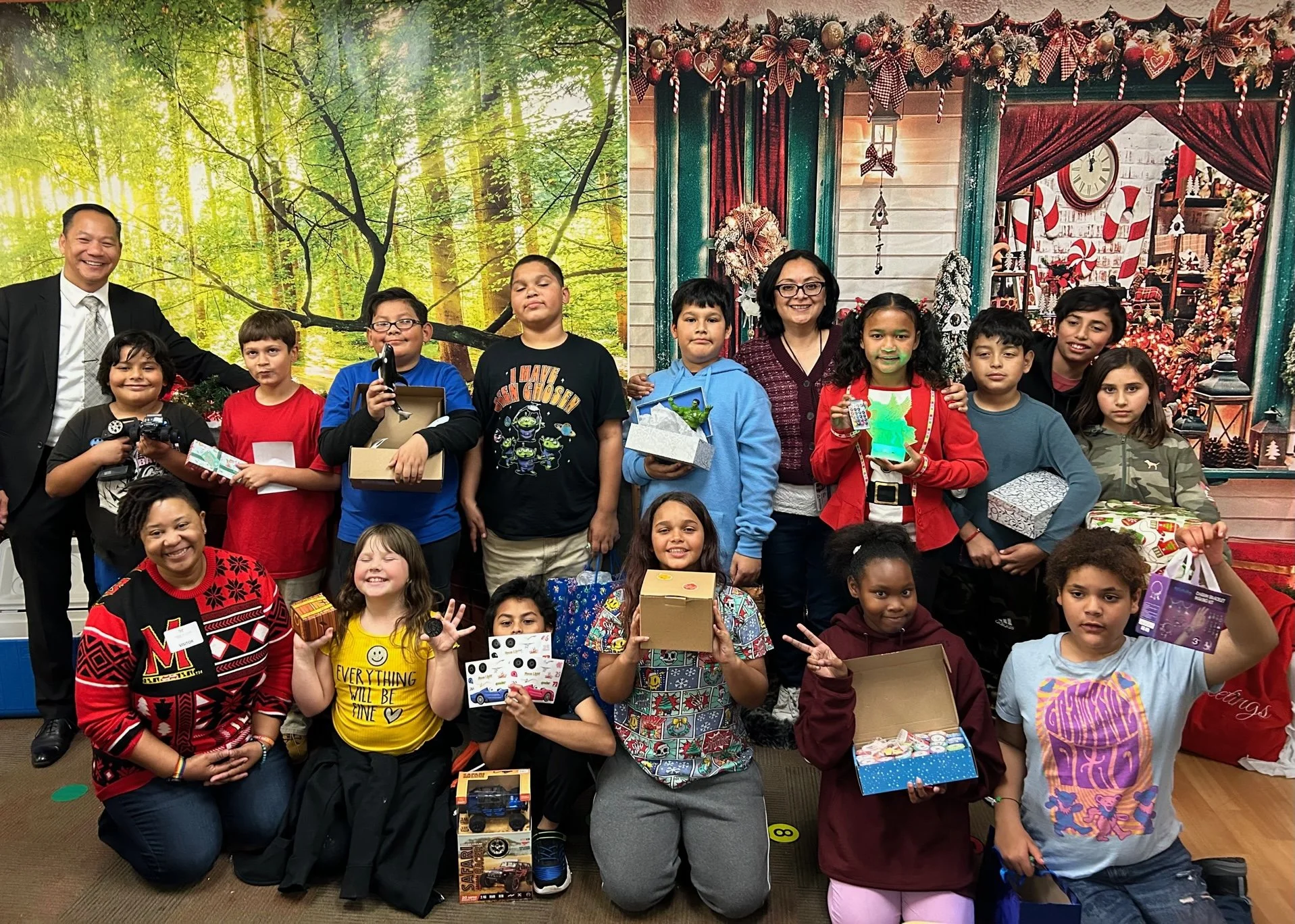 Group of children and two adults posing for a photo, some holding wrapped gifts, in a festive setting with holiday decorations and a Christmas themed background.