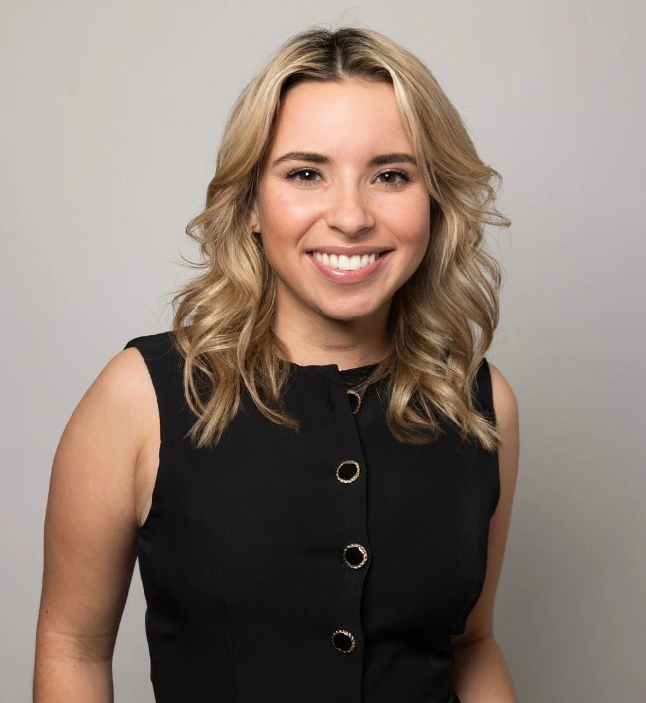 Headshot of a smiling woman with blonde wavy hair, wearing a dark blazer, against a dark background.