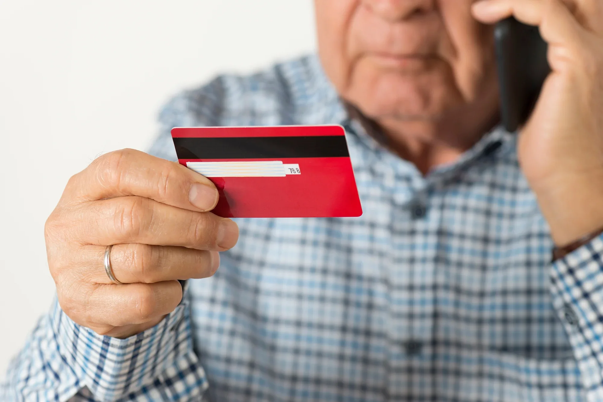 Elderly man holding a red and black credit card and a mobile phone to his ear.