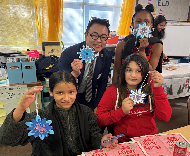 Teacher and three students in a classroom holding snowflake-shaped holiday decorations.