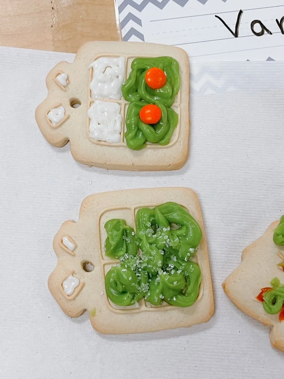 Decorated sugar cookies shaped like toasters with green frosting 'toast' and orange candy 'slices.'