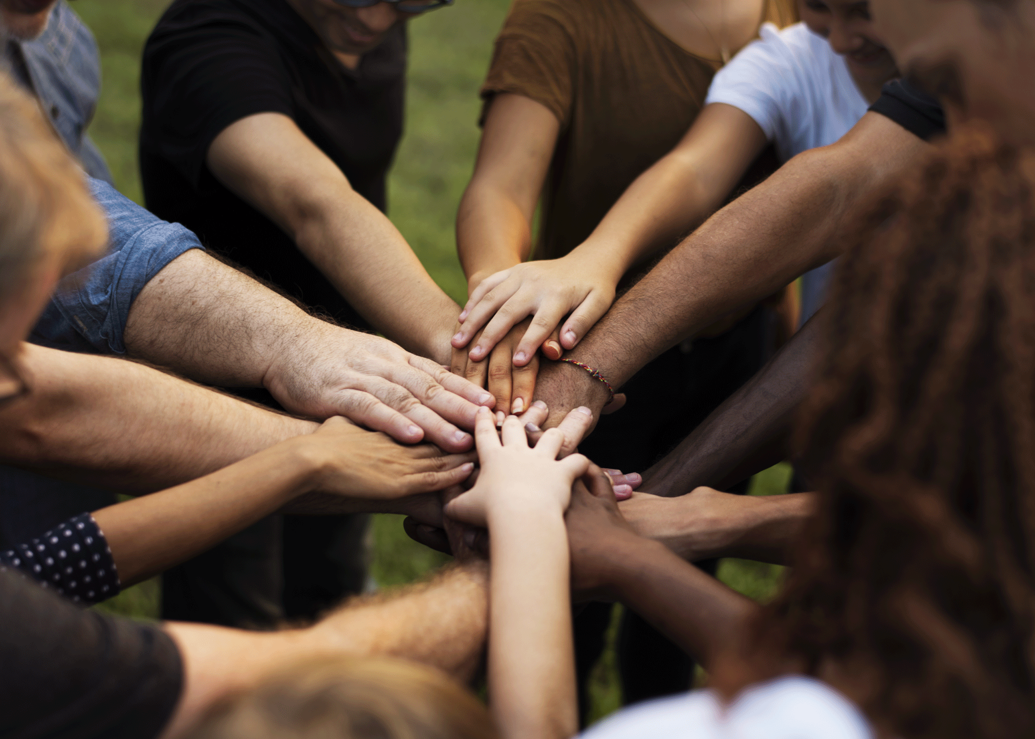Group of diverse people with their hands stacked together in the center outdoors.