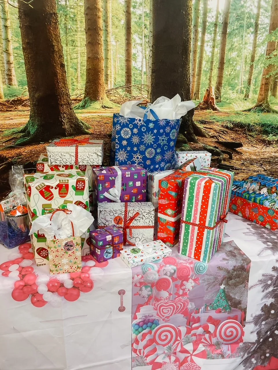 A collection of Christmas presents wrapped in colorful holiday paper, arranged on a table with a forest backdrop.