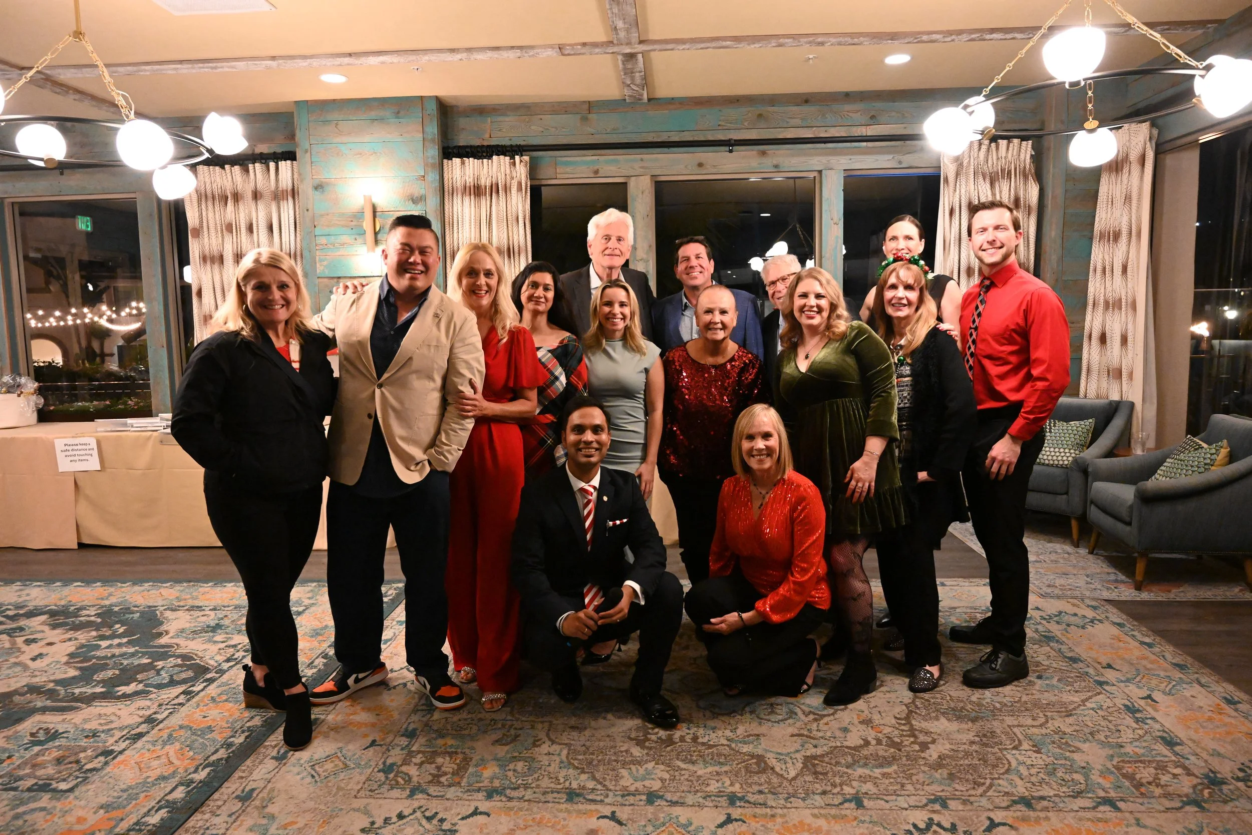 A group of 15 people posing together indoors, dressed in festive and formal attire, with some wearing holiday-themed accessories, in a decorated room.