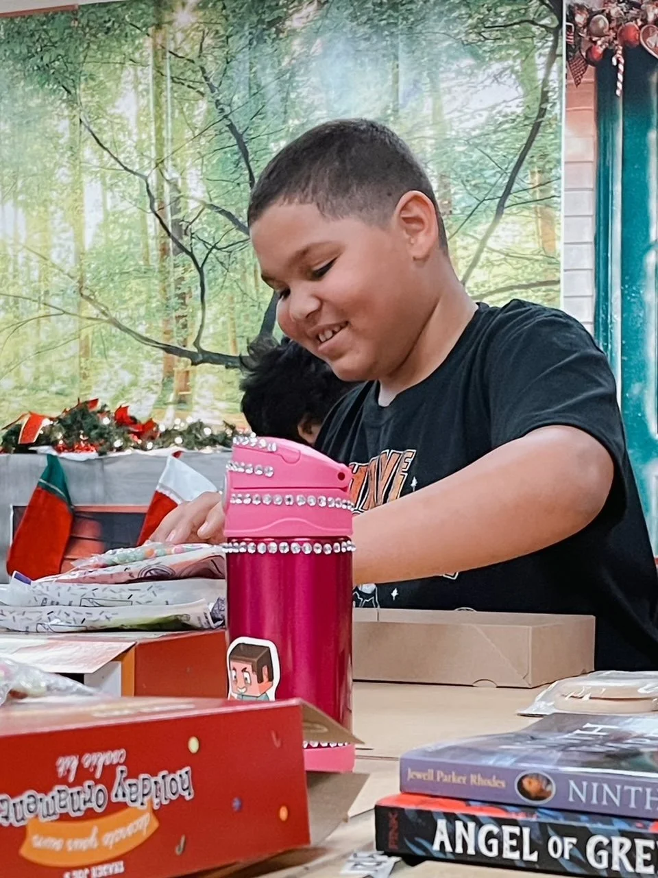 A young boy opening Christmas presents, surrounded by gift boxes and holiday decorations, with a forest-themed backdrop.