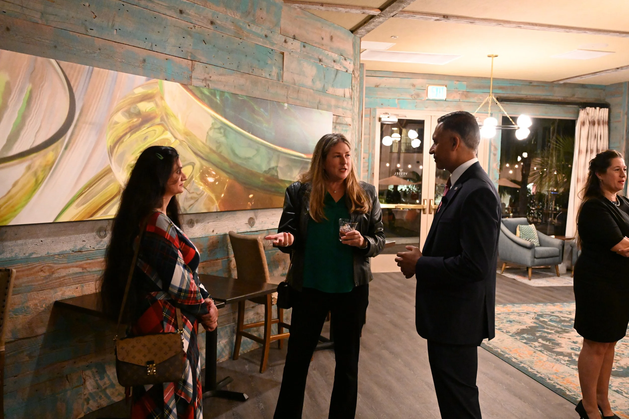 Group of four people engaged in conversation in a cozy, modern indoor space with wooden walls, artwork, and contemporary furniture.