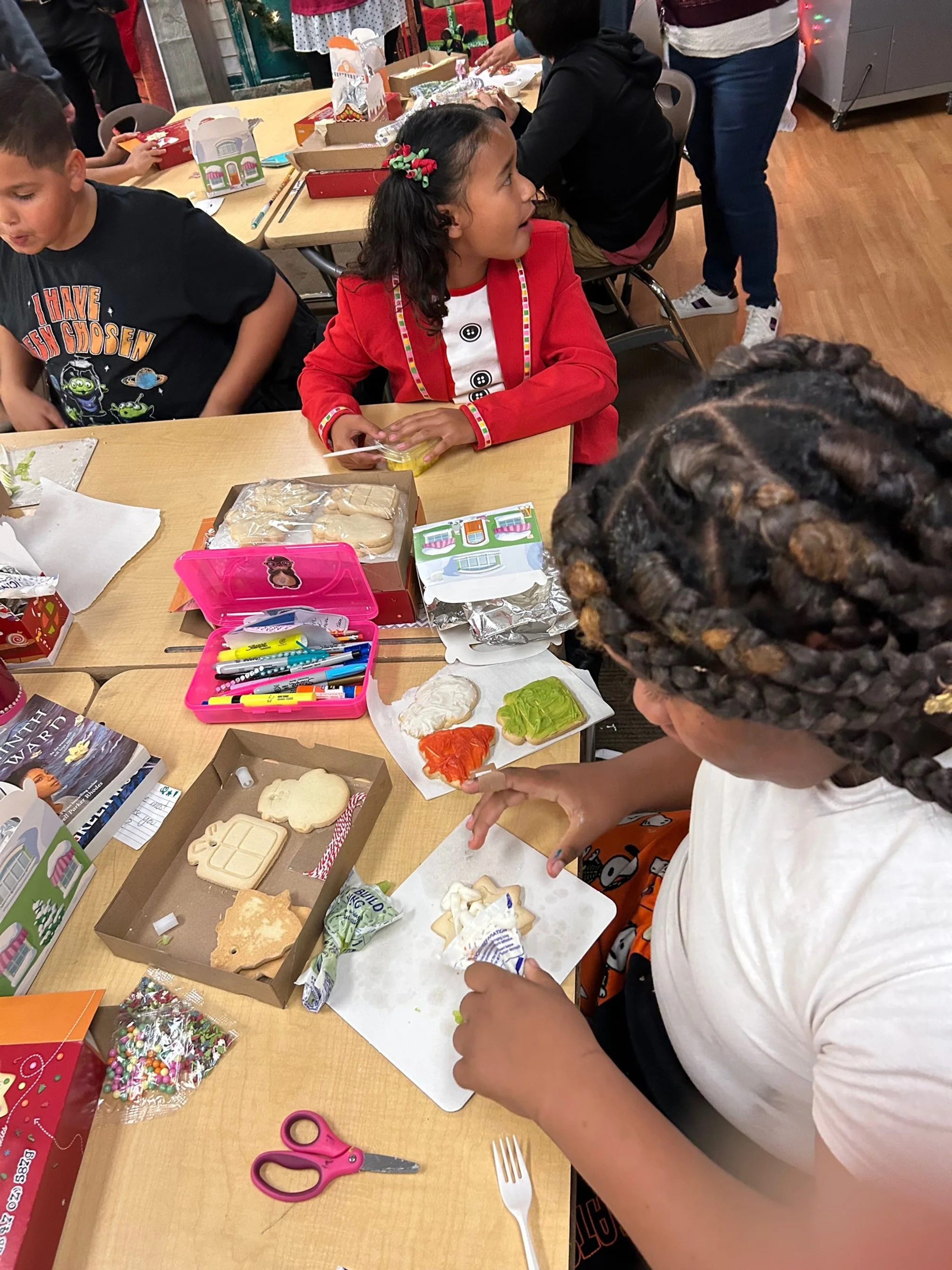 Children decorating cookies at a holiday party, with various decorated cookies, markers, and frosting on the table.