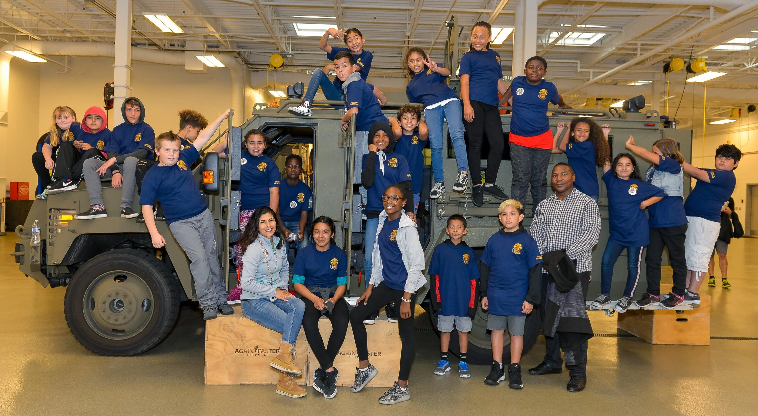 Group of children and adults posing on and around a large fire truck inside a fire station.