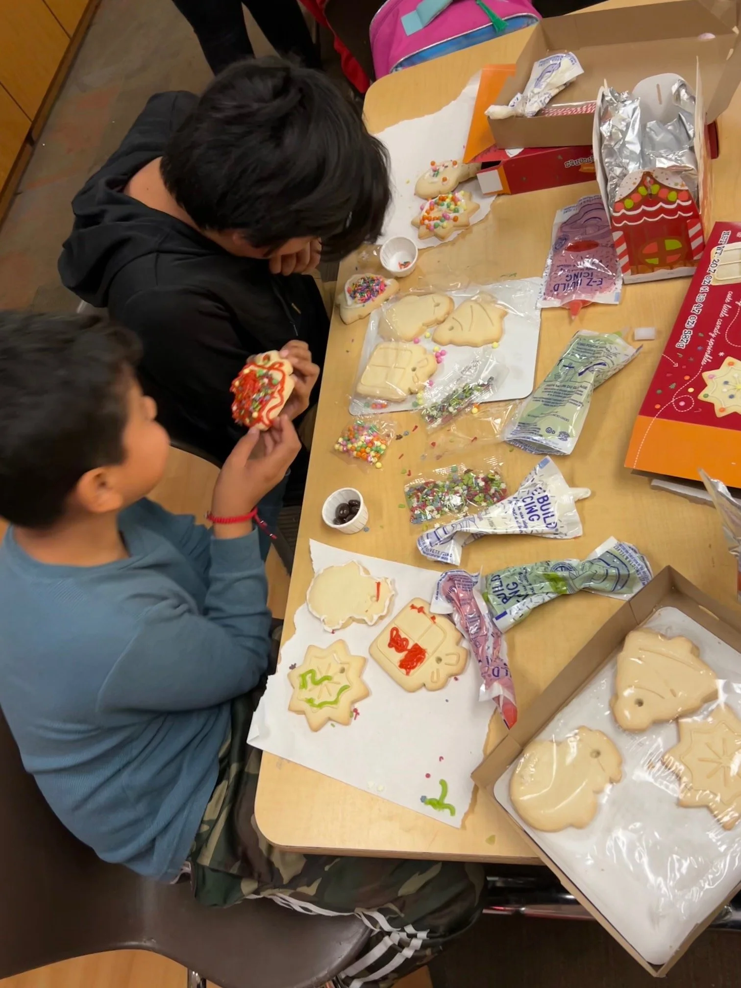 Children decorating Christmas cookies with sprinkles, icing, and candies on a table with various cookies and decorating supplies.