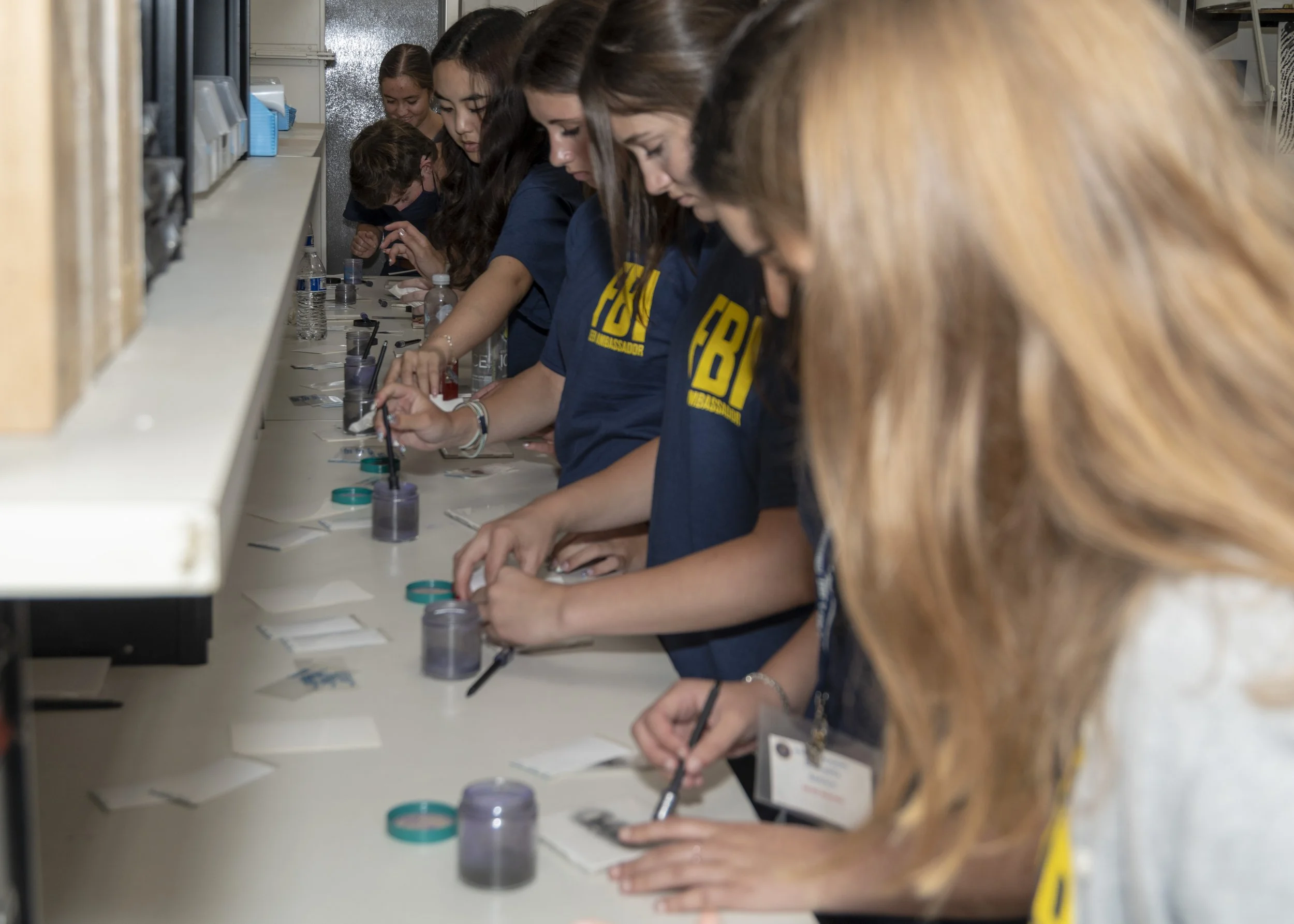 A group of young women working at a scientific laboratory bench, conducting experiments with small containers and tools.