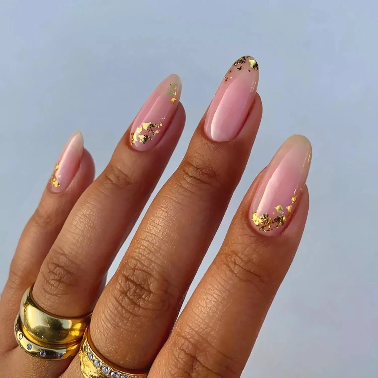 Close-up of a woman's hand with natural skin tone, displaying nails with a light pink base and gold foil accents at the tips.