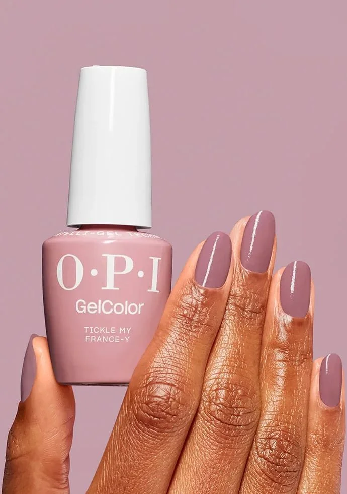 A hand with neatly manicured nails holding a bottle of pink O.P.I gel nail polish labeled 'Tickle My France-Y'. The nails are painted in a soft pinkish-mauve color with a thin white line down the center.