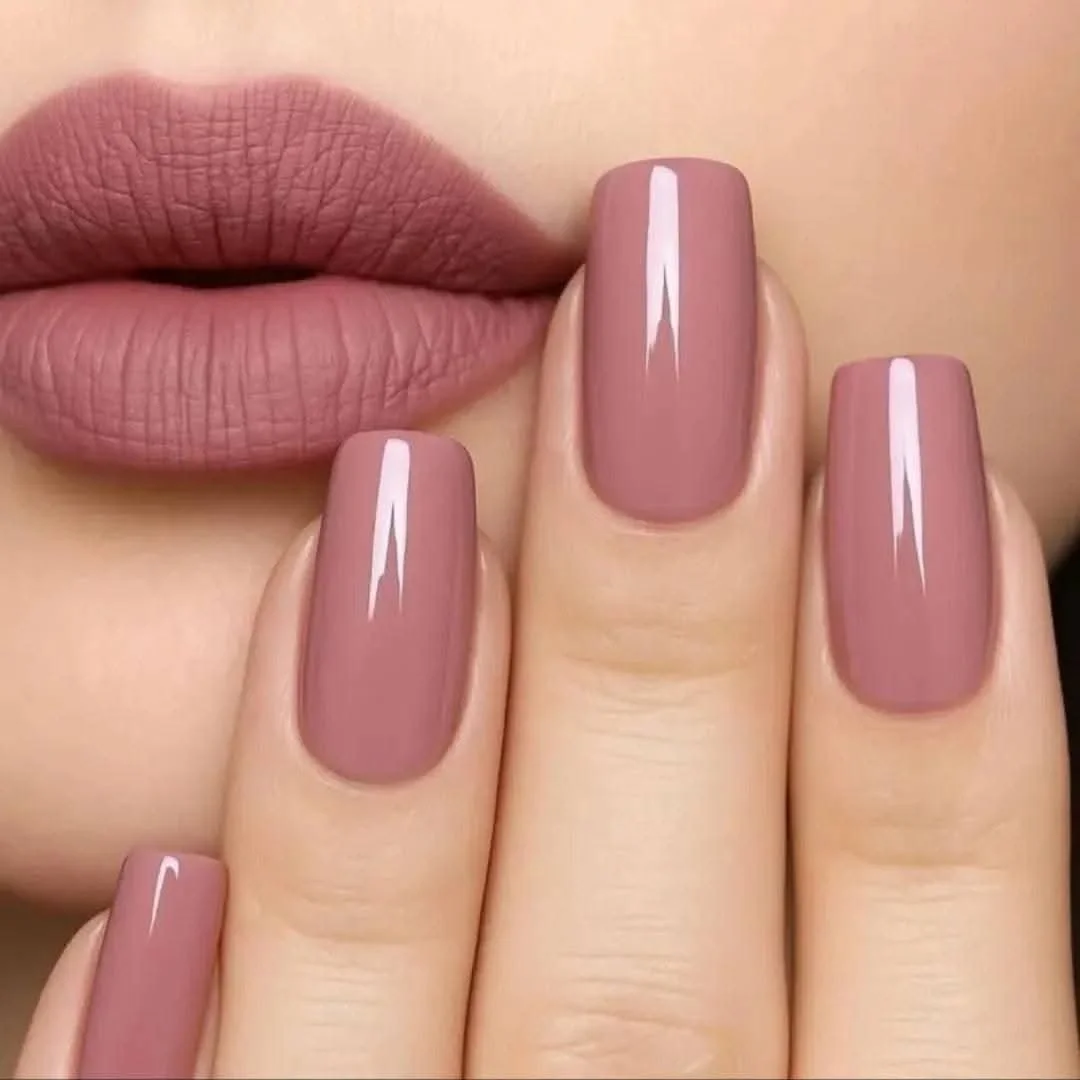 Close-up of a person's lips with matte pink lipstick and nails painted with matching taupe-colored nail polish, with a glossy finish.