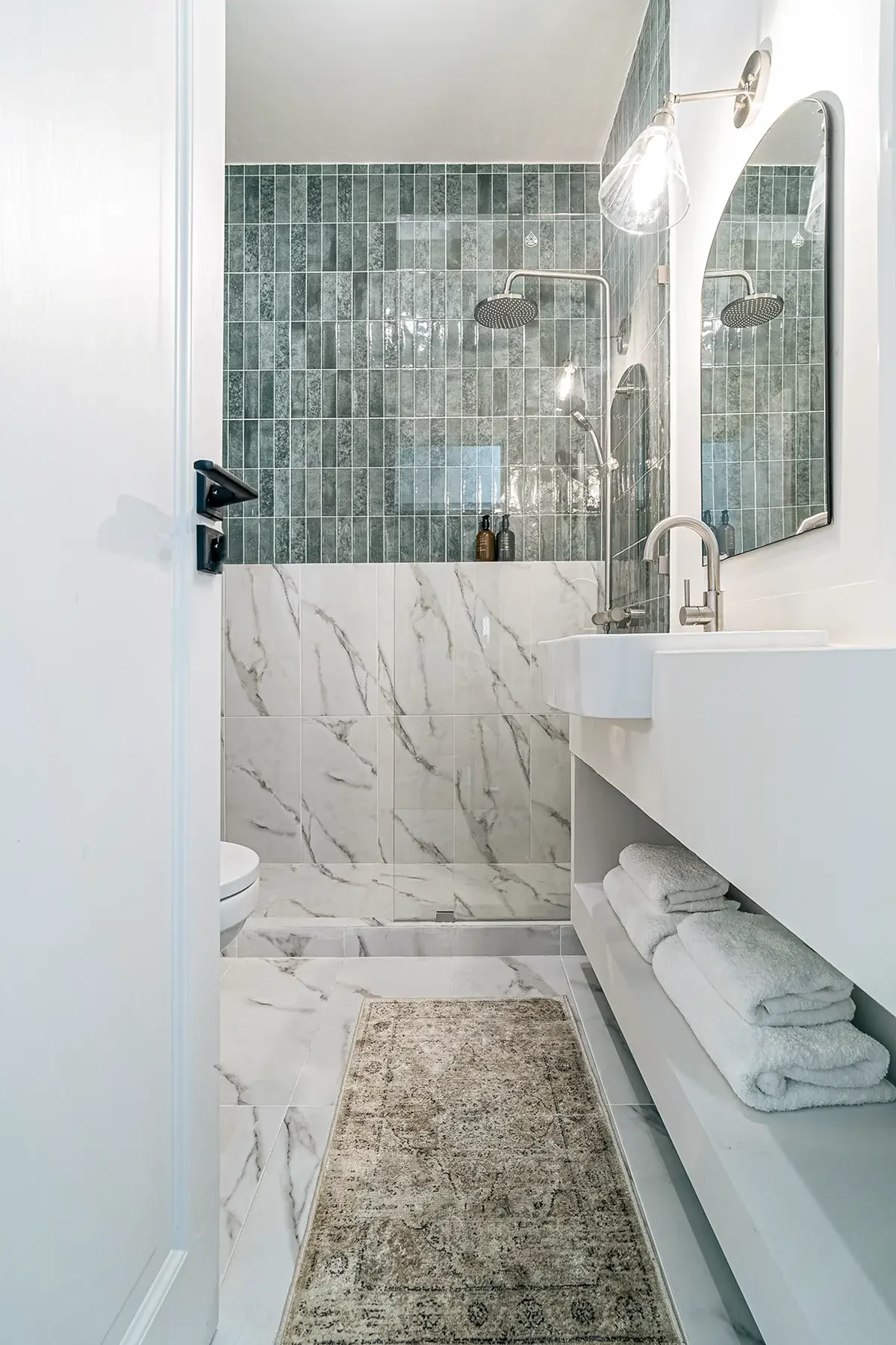 Luxury bathroom in Studio 51 with marble and green tiled shower, white sink, towel rack and walk-in double showerheads.