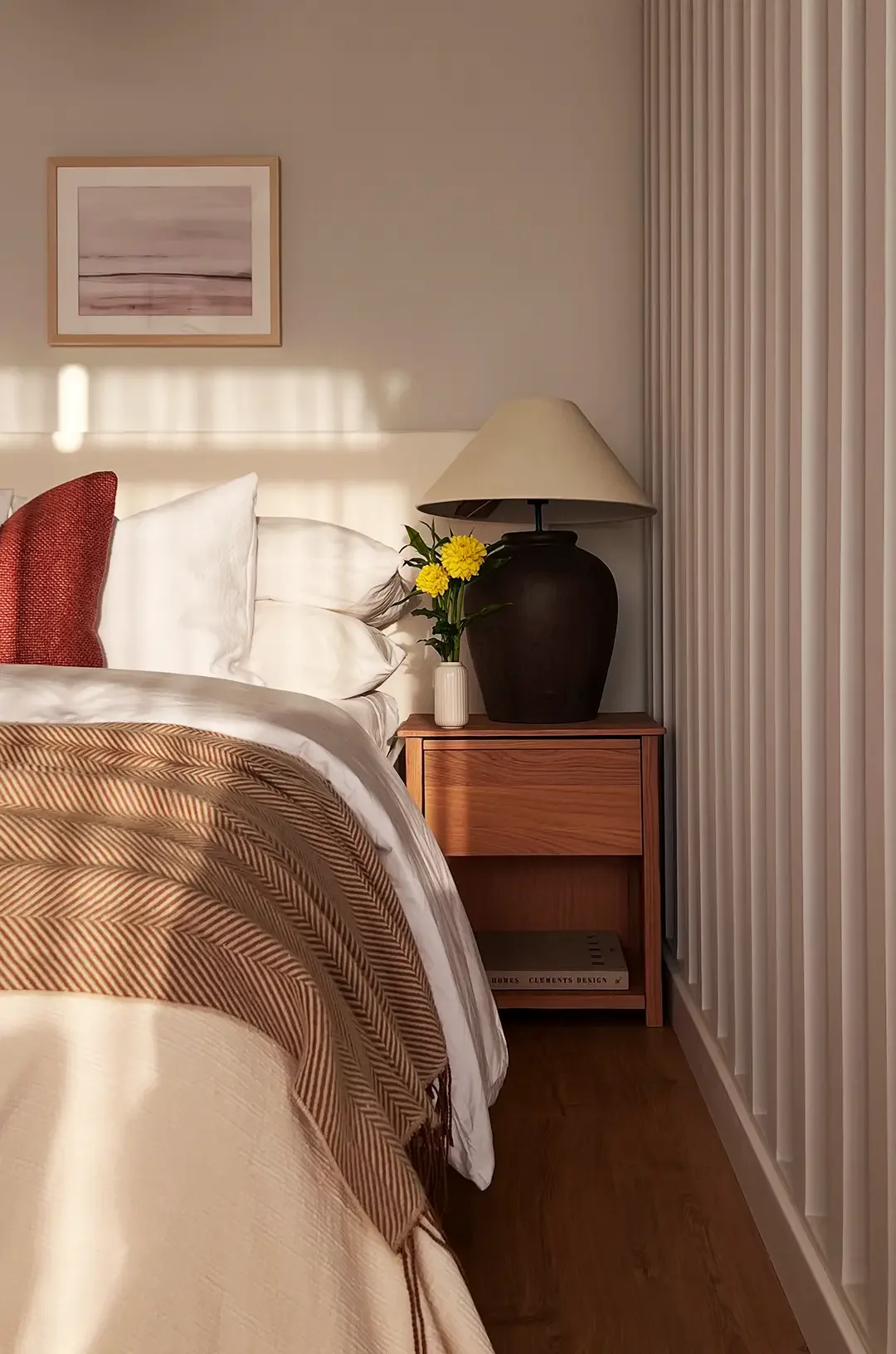 Bedroom detail with black table lamp, ceramic vase, yellow flowers and framed artwork, styled by Studio Sakaia.